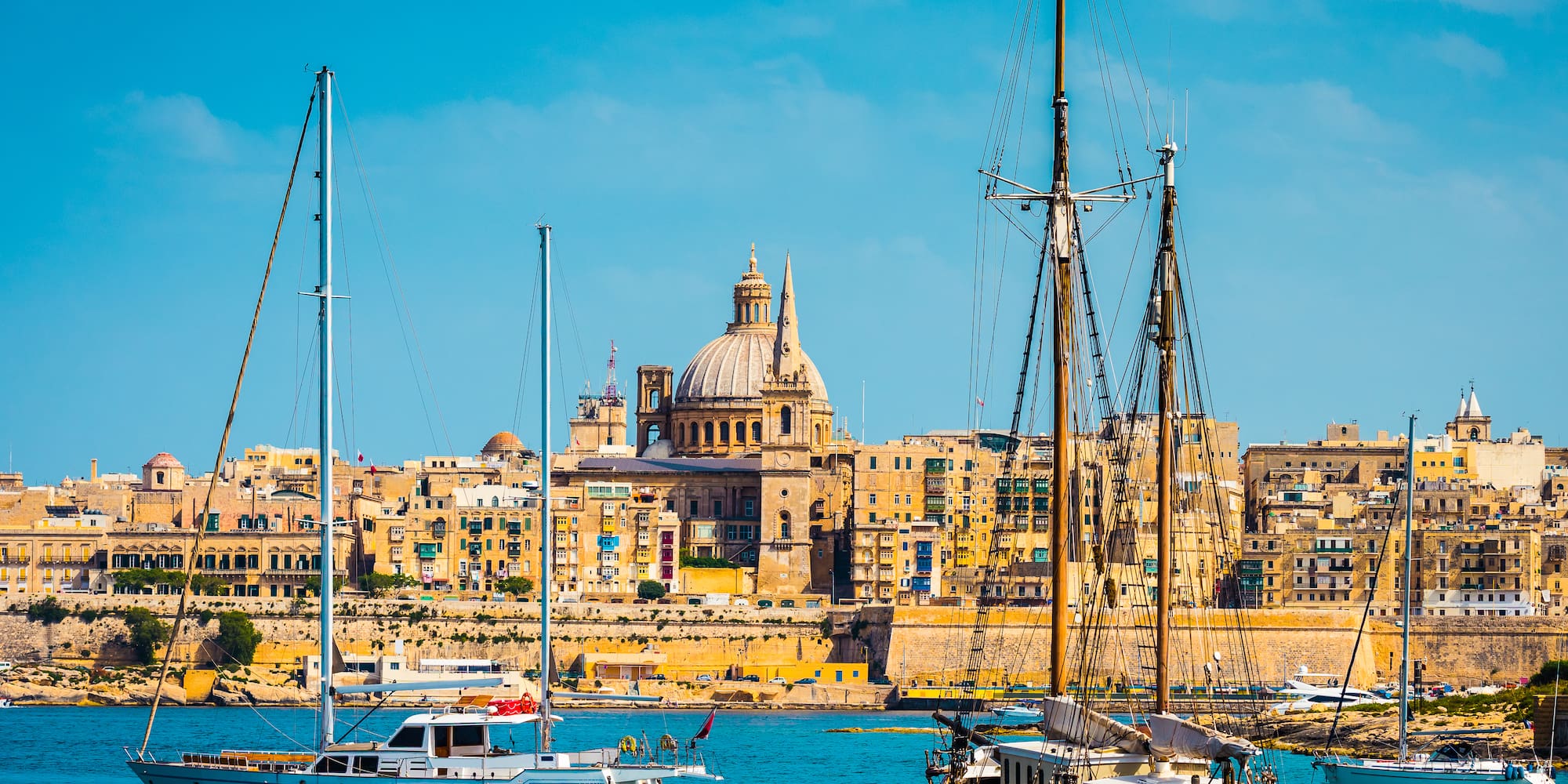Boats in Valletta harbor with historic city skyline and a prominent dome, Malta.