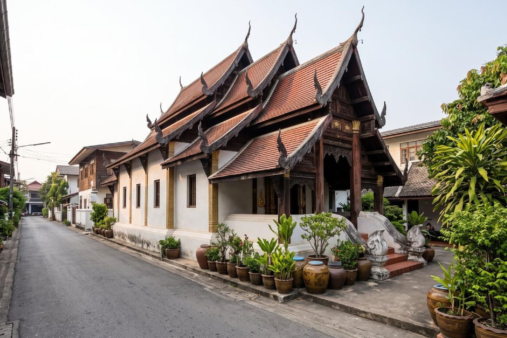 Ornate Thai temple with tiled roof and white walls on a quiet street.