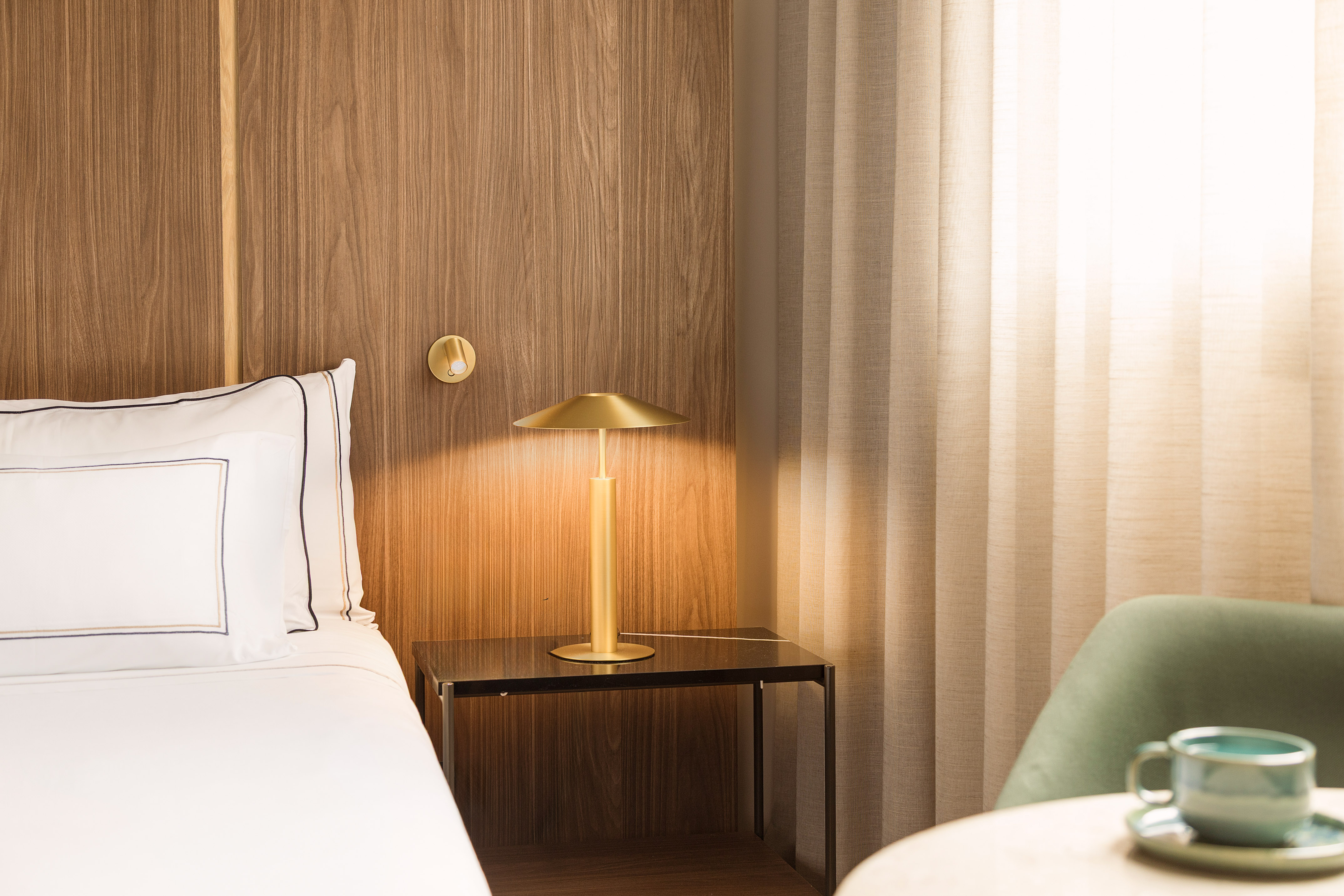 Modern hotel bedroom with wooden headboard, bedside lamp, and cozy seating area.
