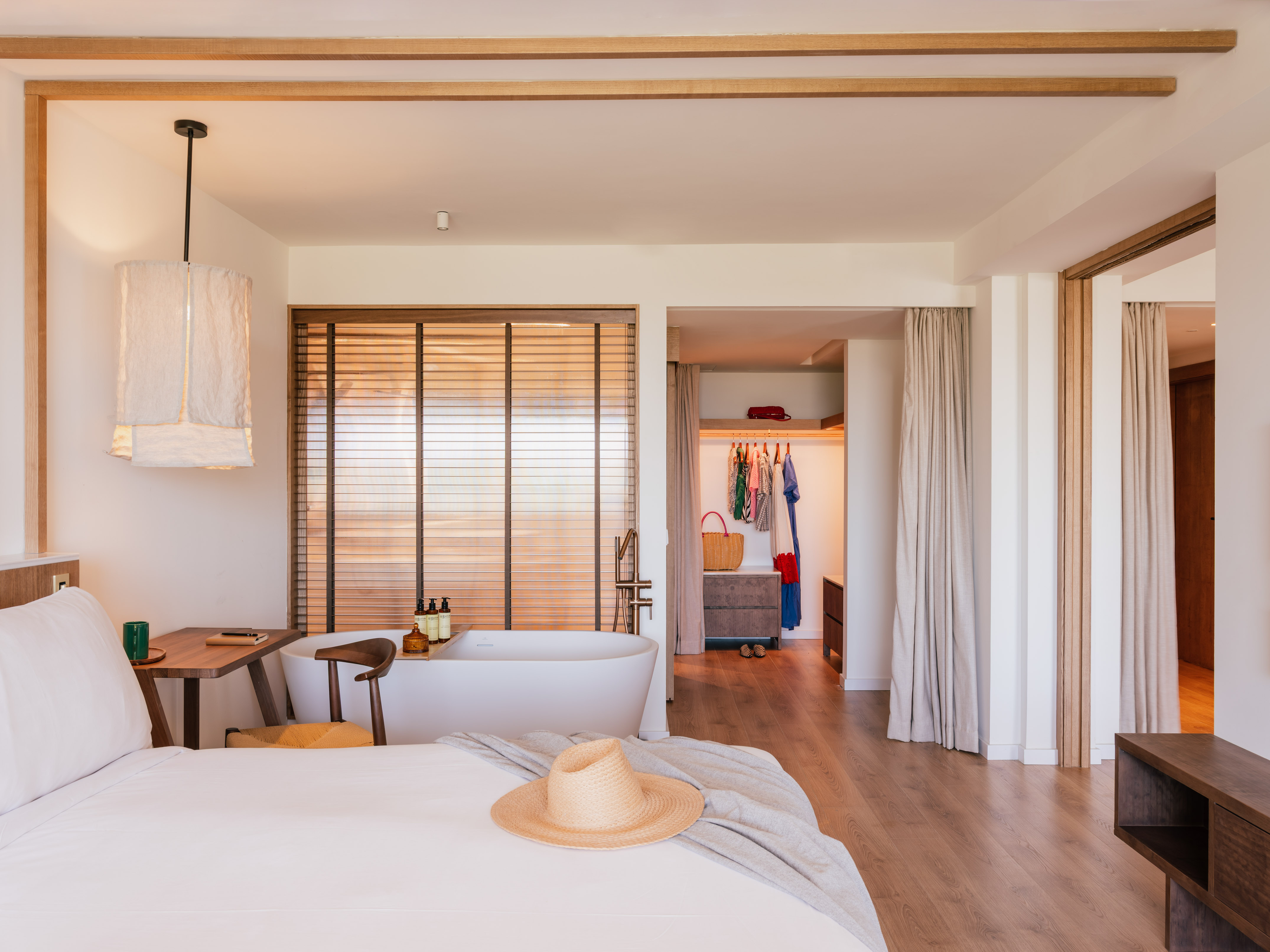 Modern resort bedroom with freestanding bathtub, large bed, and straw hat.
