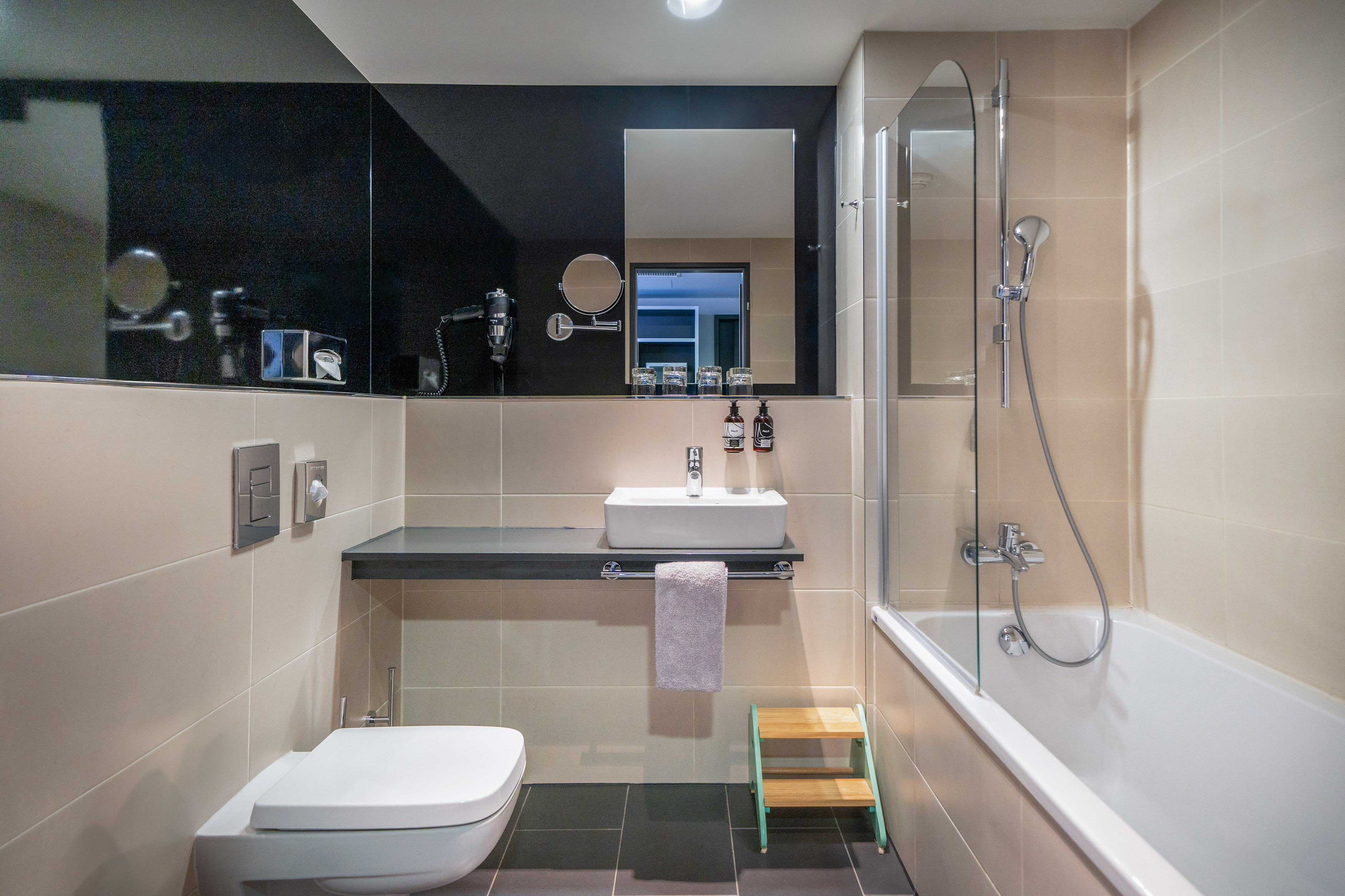 Modern bathroom with white toilet, sink, bathtub, and beige tiles. - The INNSiDE Room for Families - Innside Berlin Mitte, Berlijn