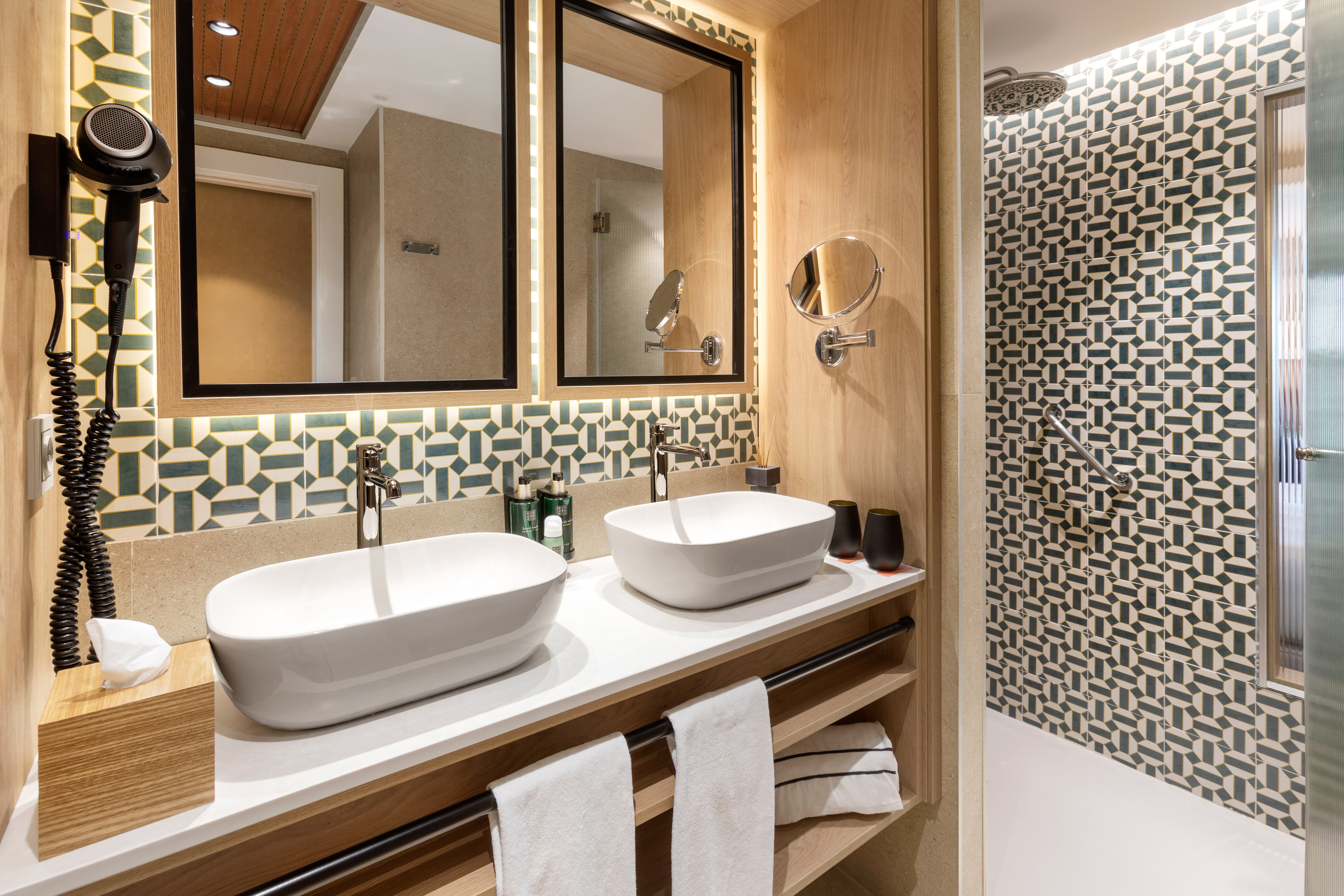 Modern double vanity with white vessel sinks, wood, and geometric tile backsplash.