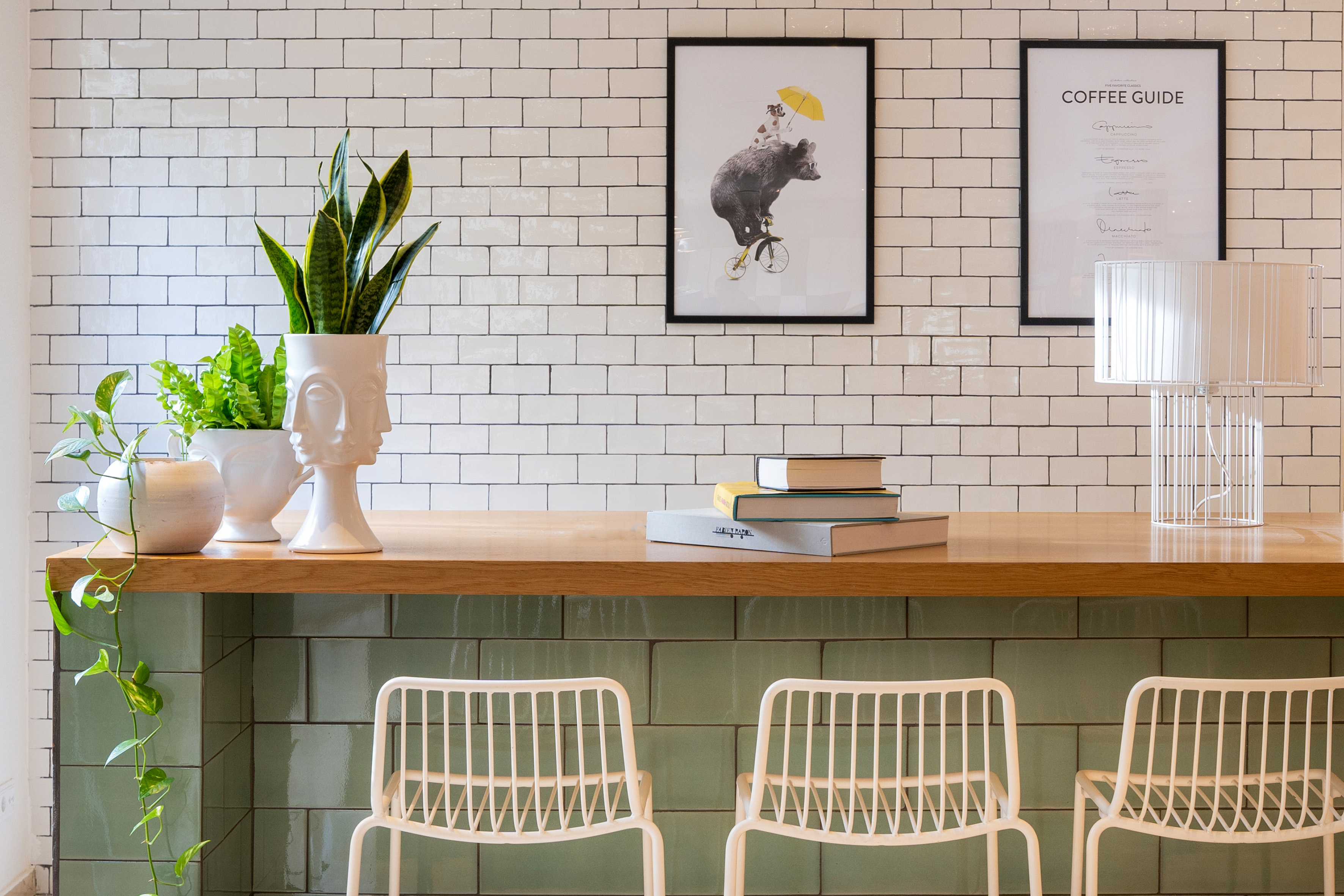 Modern cafe counter with plants, white subway tiles, coffee guide, and art.