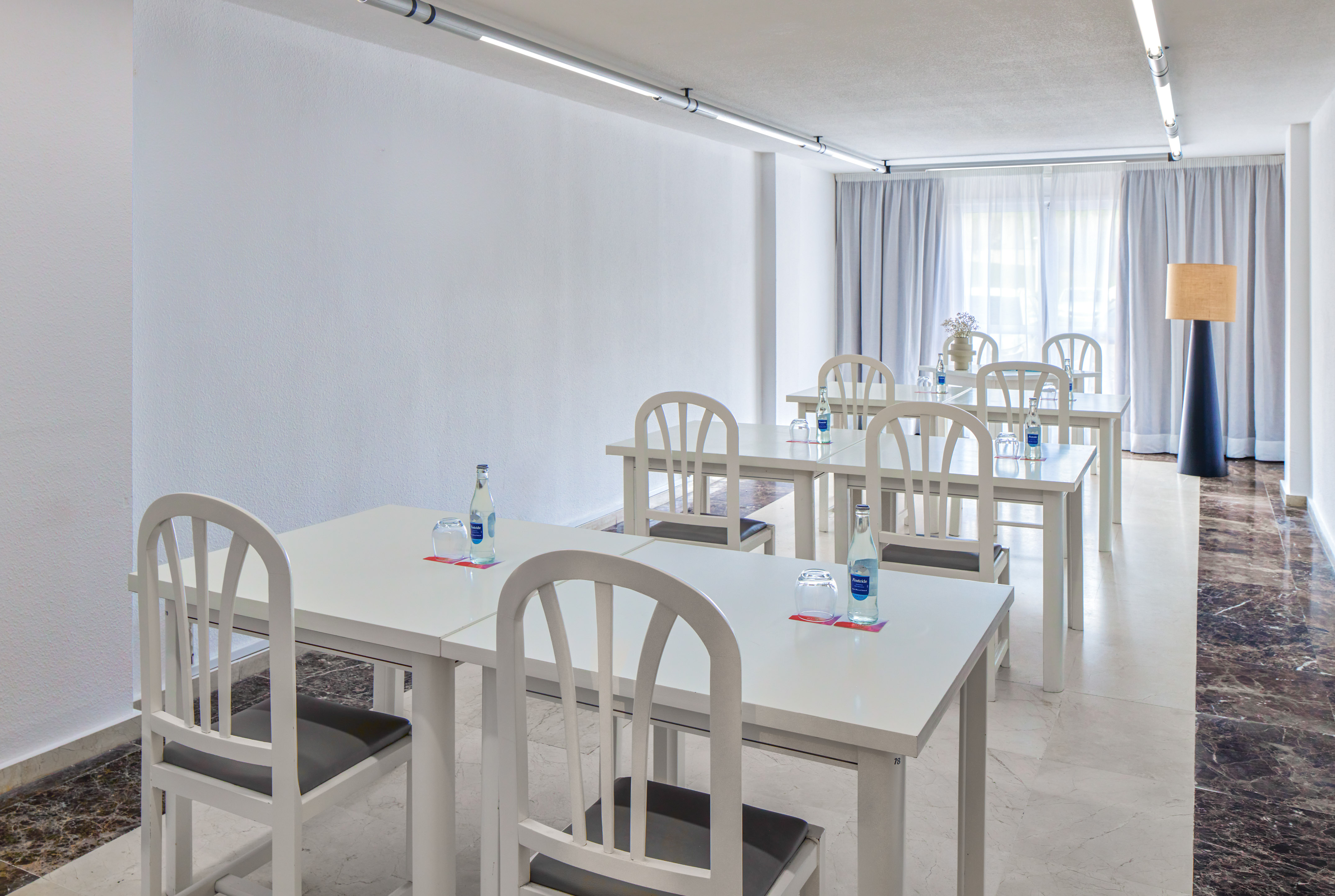 Modern conference room with white tables, chairs, and bottled water for meetings.