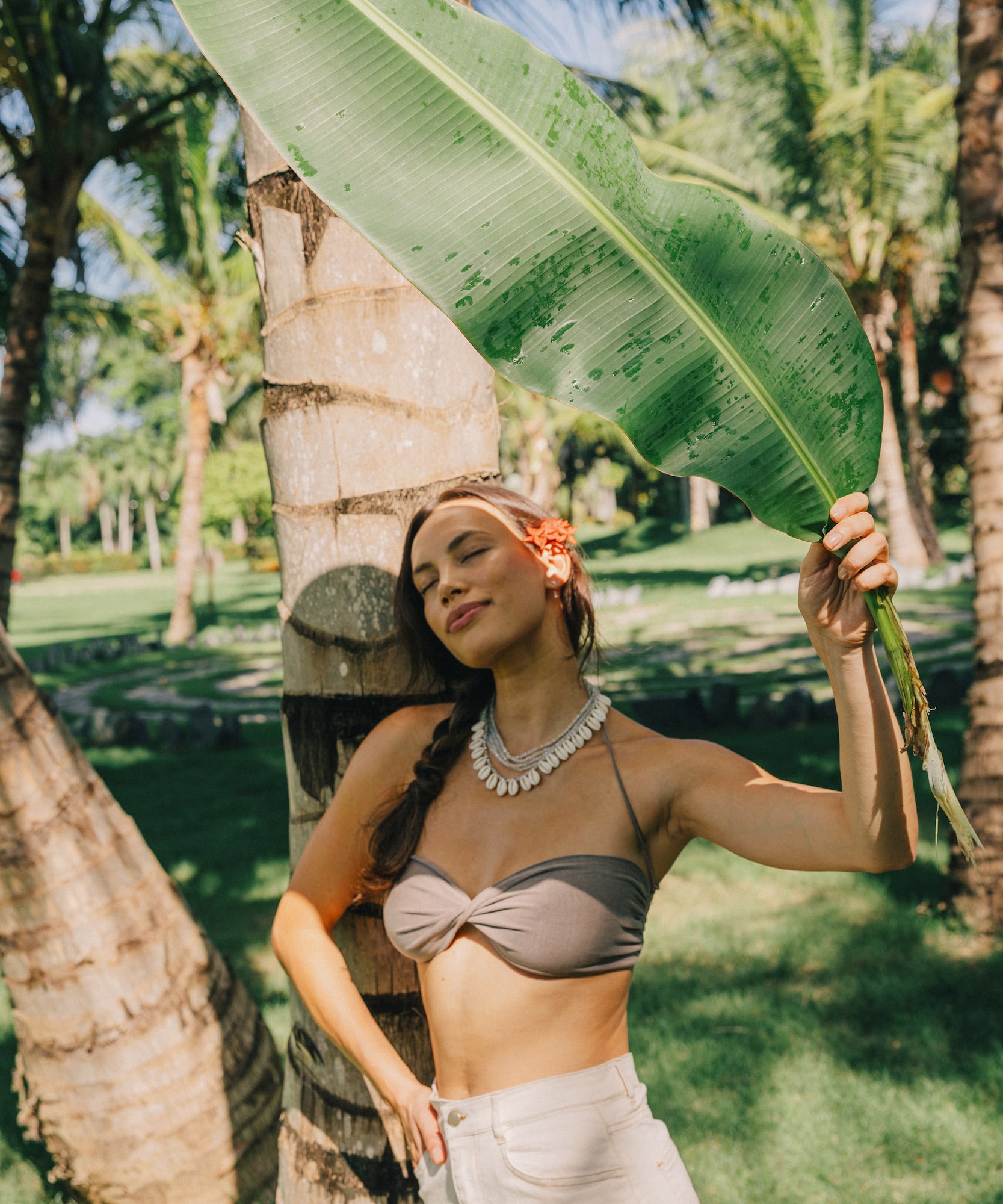 Tropical woman holding banana leaf for shade by palm tree.