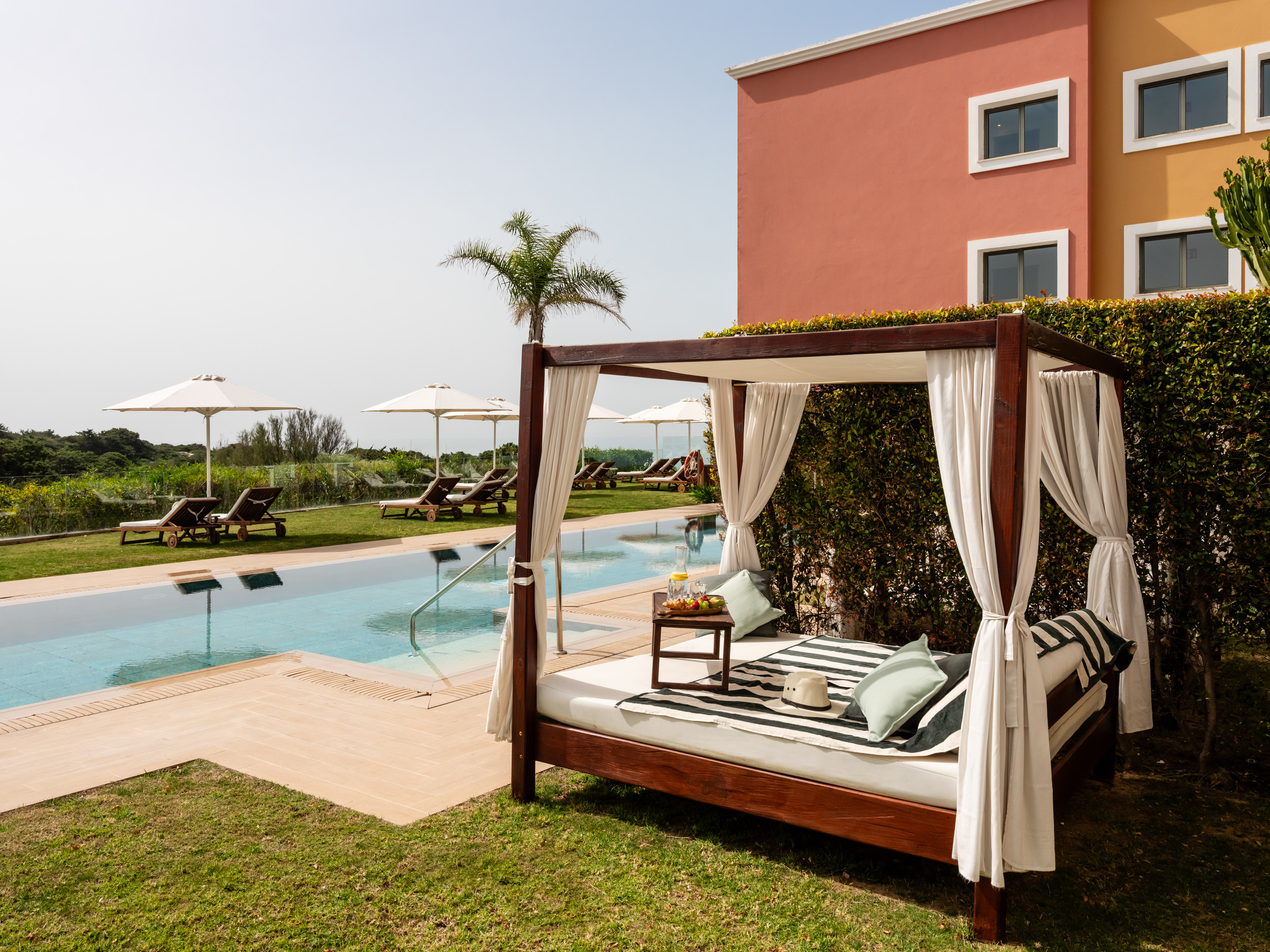 Private poolside daybed with refreshments, sun loungers, and a colorful hotel.