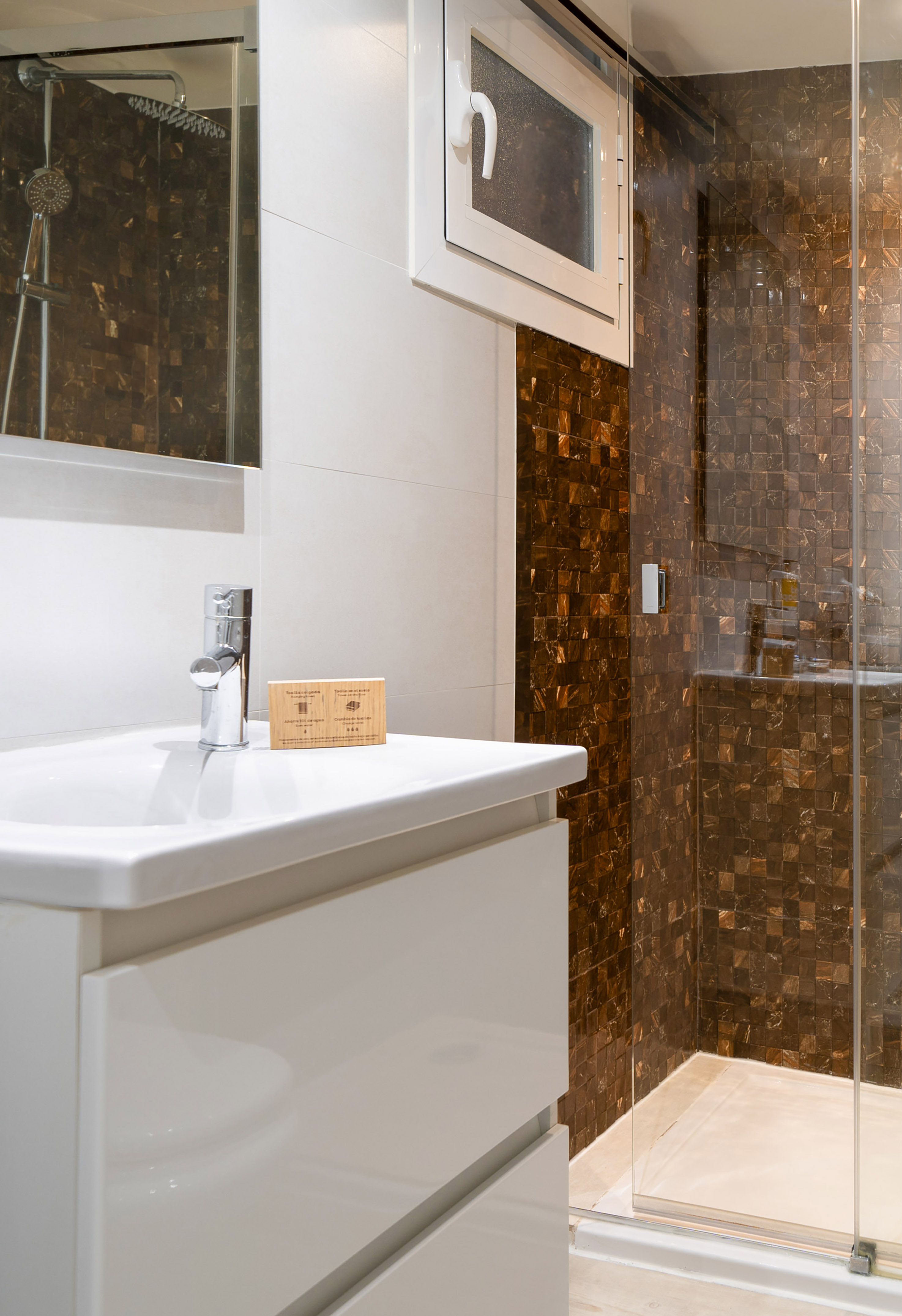 Modern bathroom with white vanity, sink, and brown mosaic tile shower.