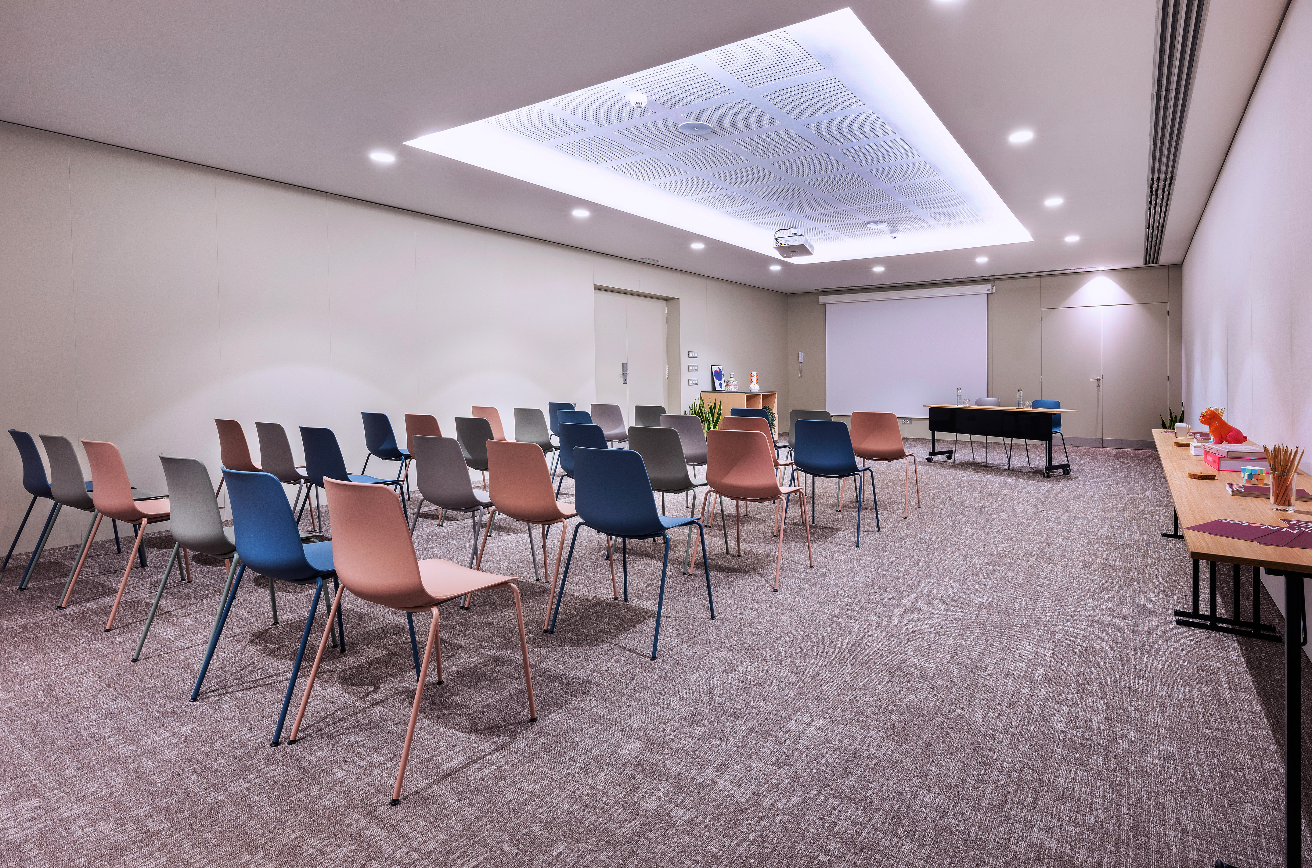 Modern meeting room with colorful chairs, projector screen, and presentation setup.