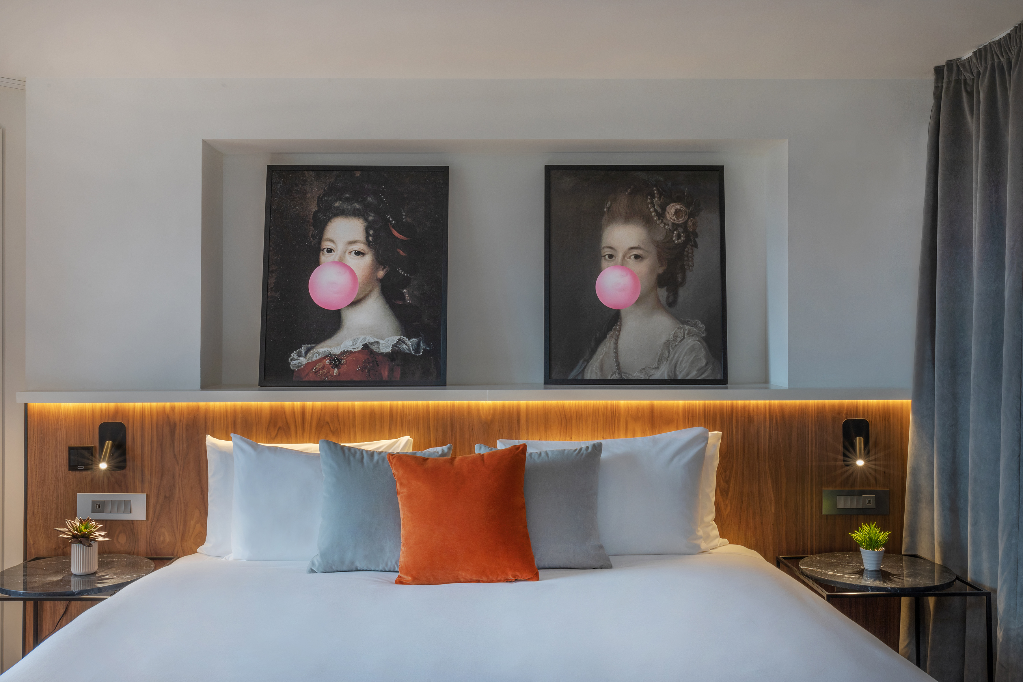 Modern hotel bedroom with pop art bubblegum portraits, wood headboard, orange pillow.