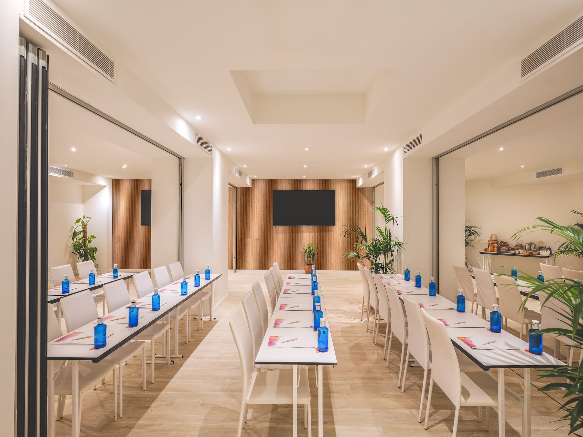 Modern conference room setup with rows of tables, blue bottles, and large screen.
