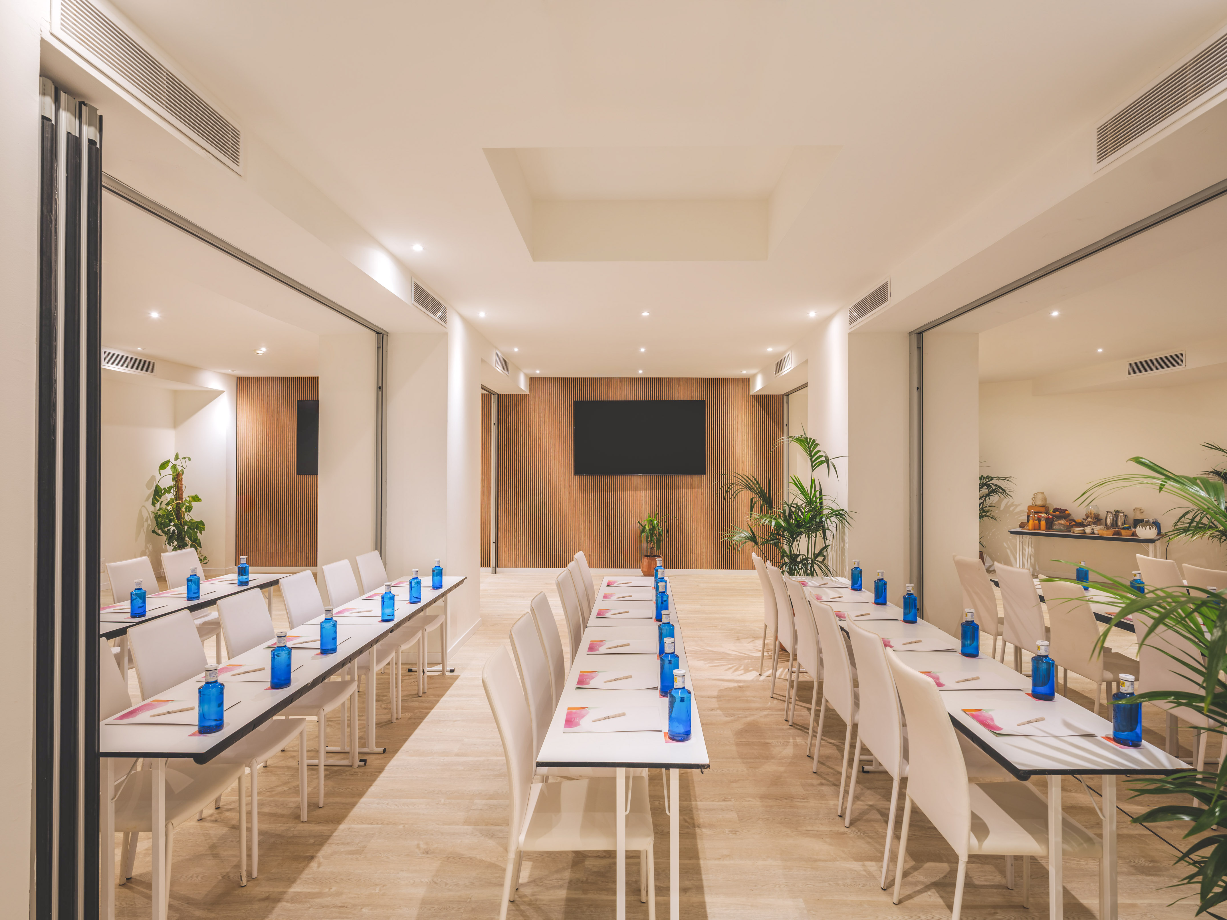 Modern conference room setup with rows of tables, blue bottles, and large screen.