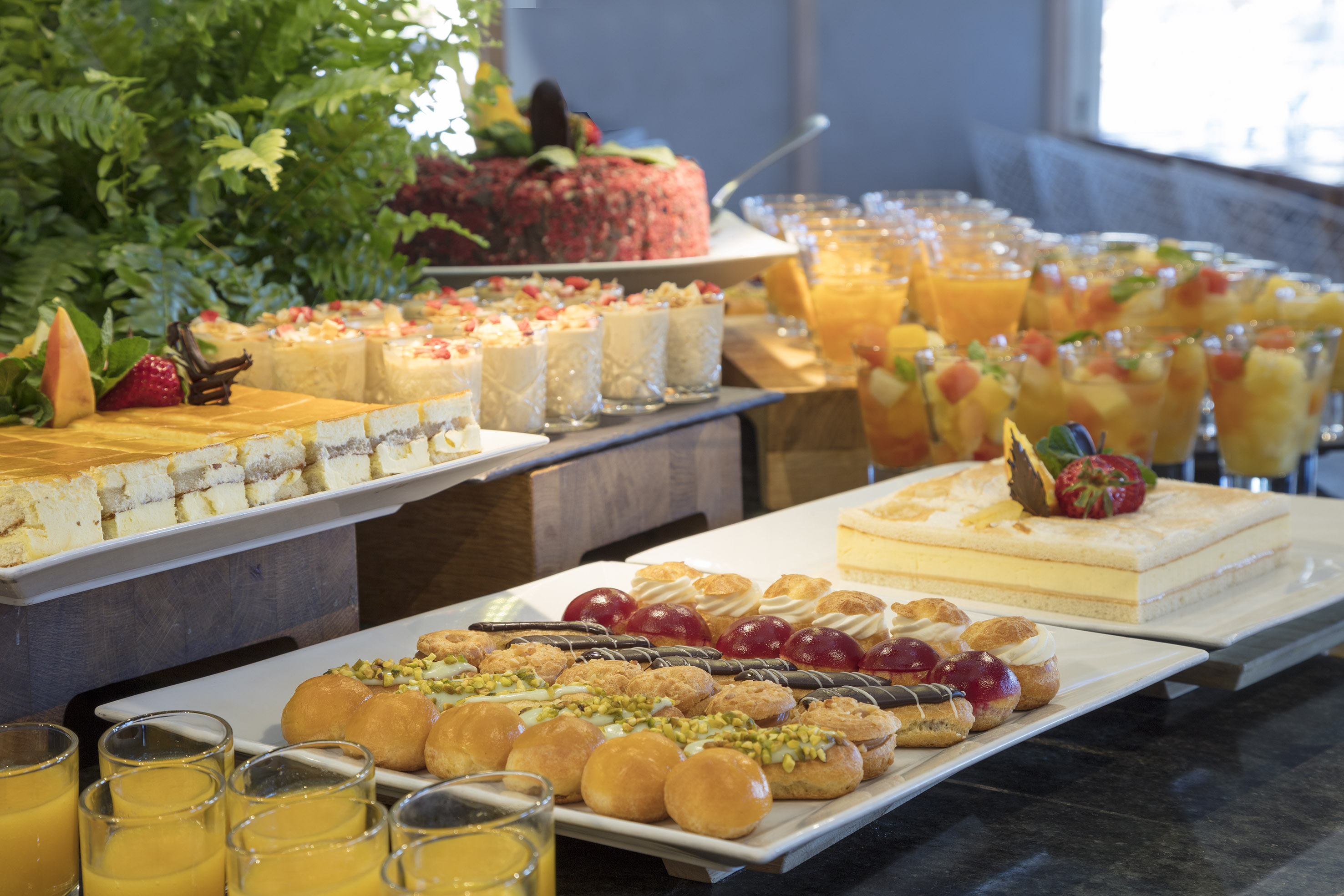 Hotel dessert buffet with cakes, pastries, fruit salads, and orange juice.
