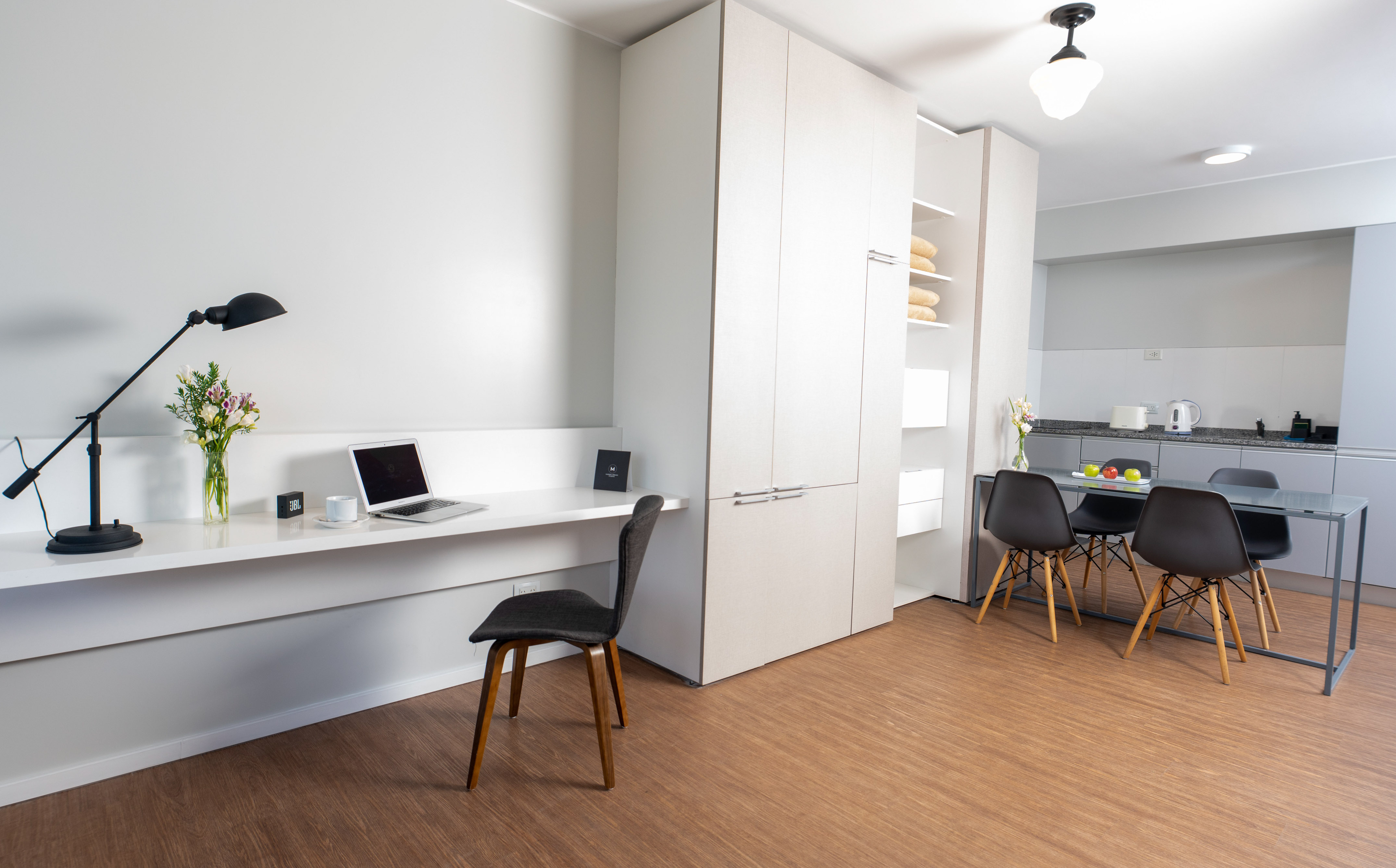Modern studio apartment with desk, dining area, and kitchenette.