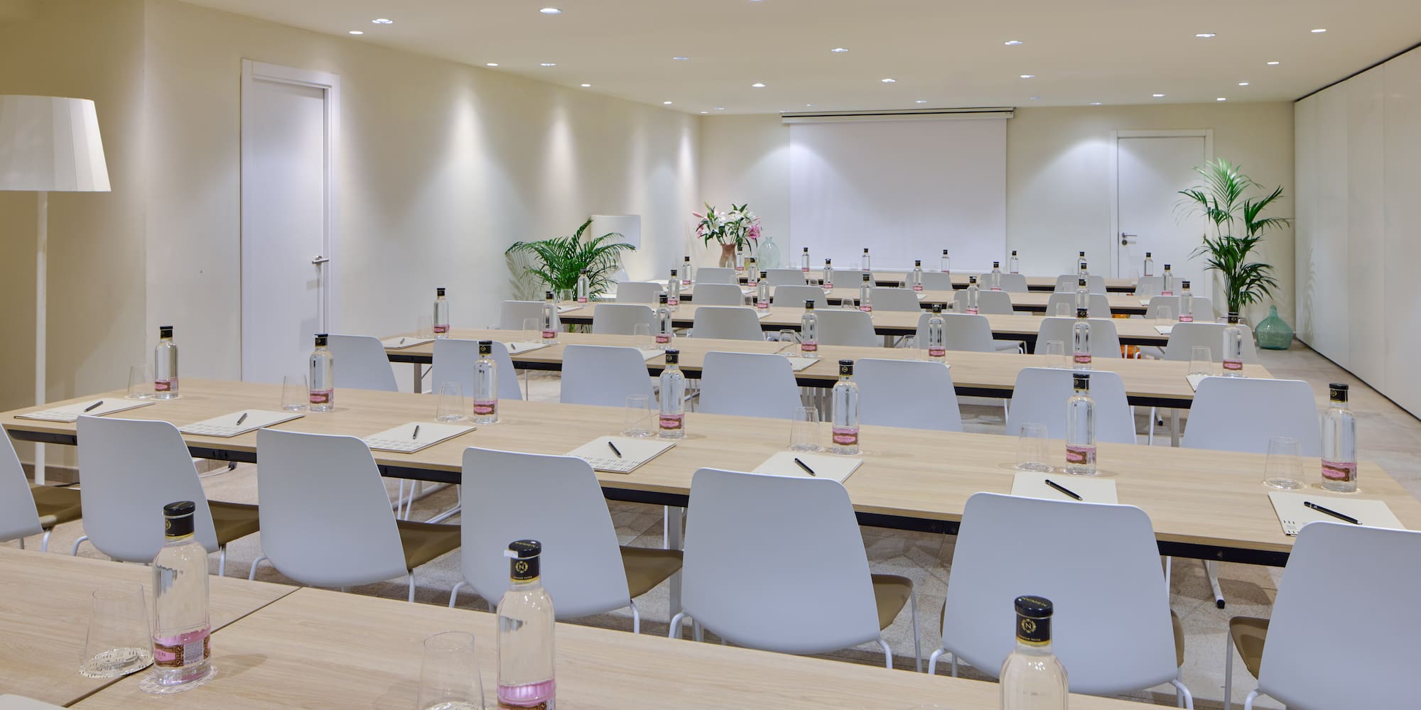 Modern conference room with tables, chairs, bottled water, and projector.