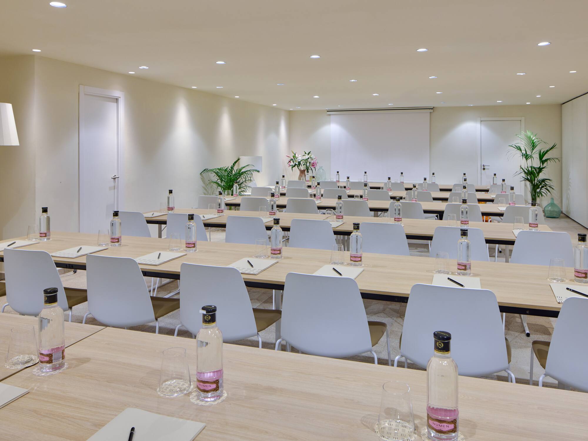Modern meeting room with light wood tables, white chairs, and screen.