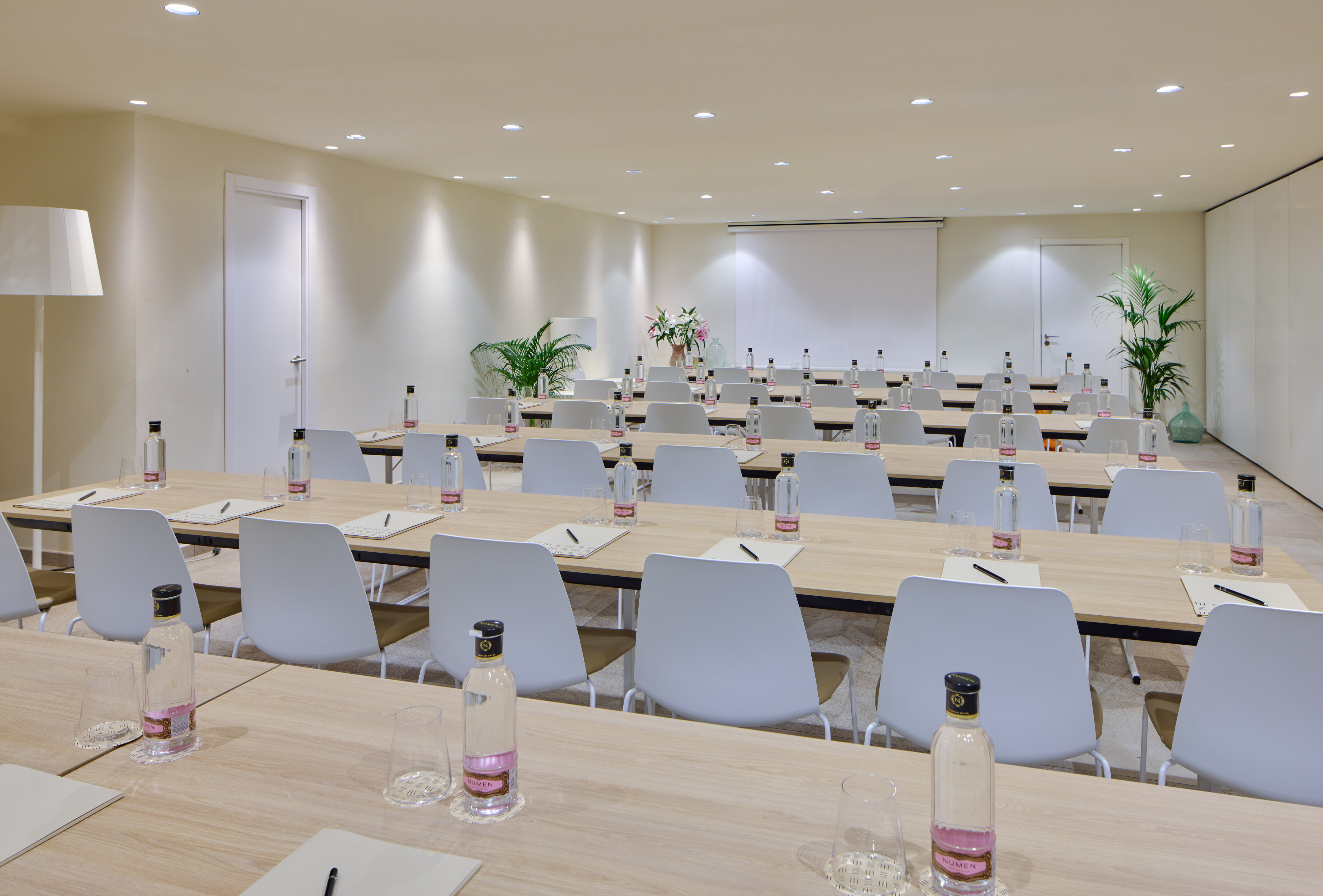 Modern meeting room with light wood tables, white chairs, and screen.