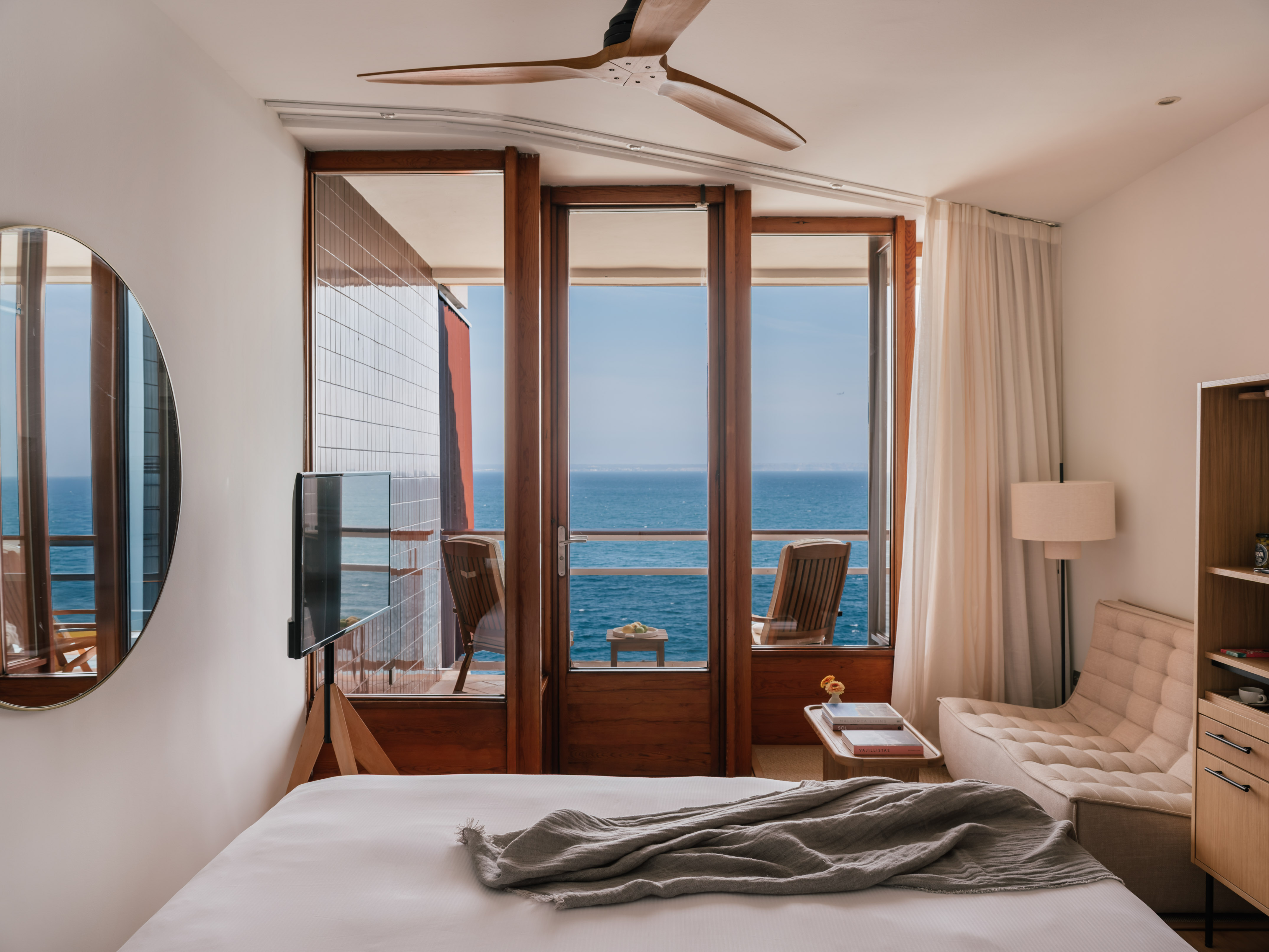 Ocean view hotel room with balcony, modern design, white bed, and ceiling fan.