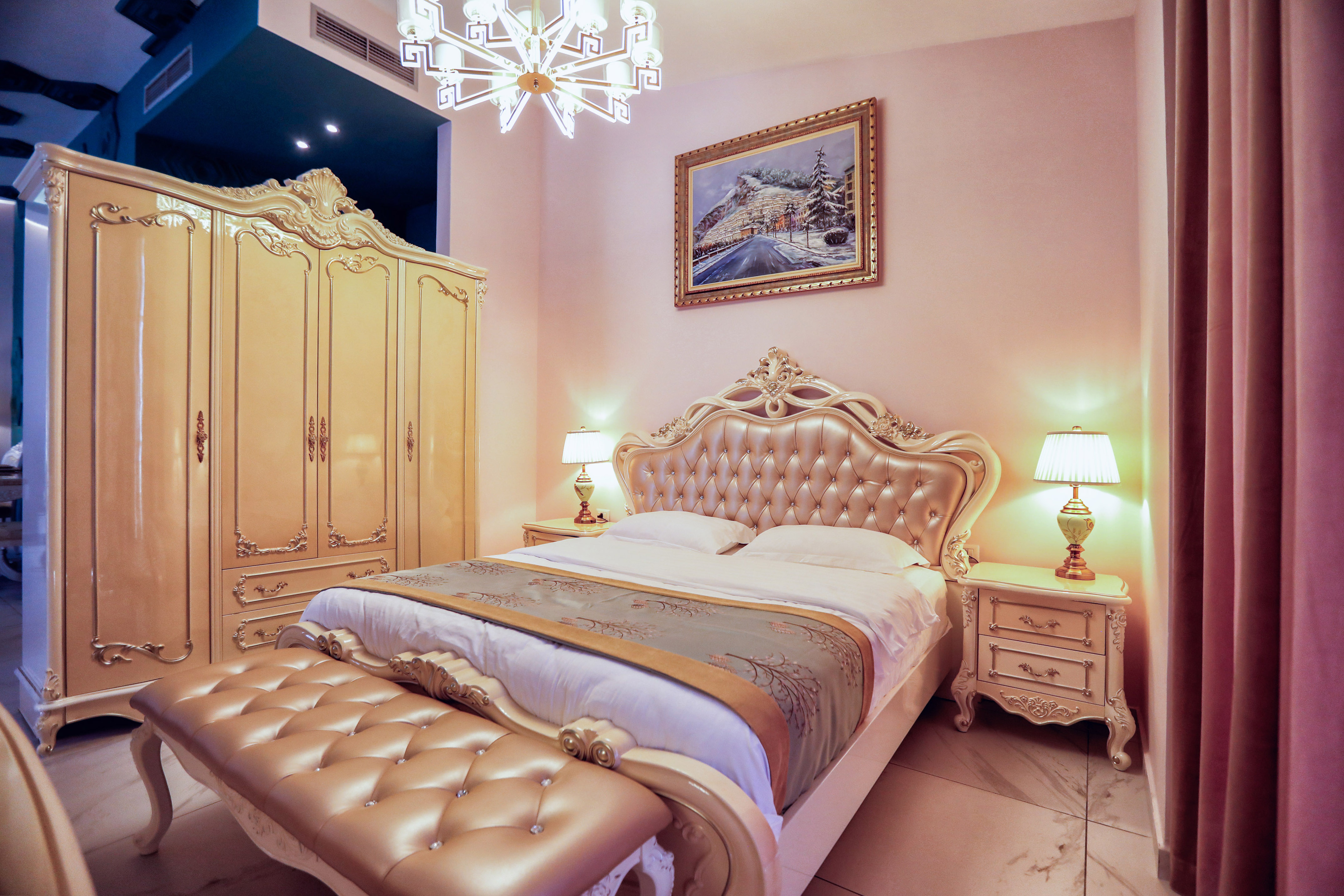 Ornate cream and gold bedroom with tufted headboard, wardrobe, and bench.