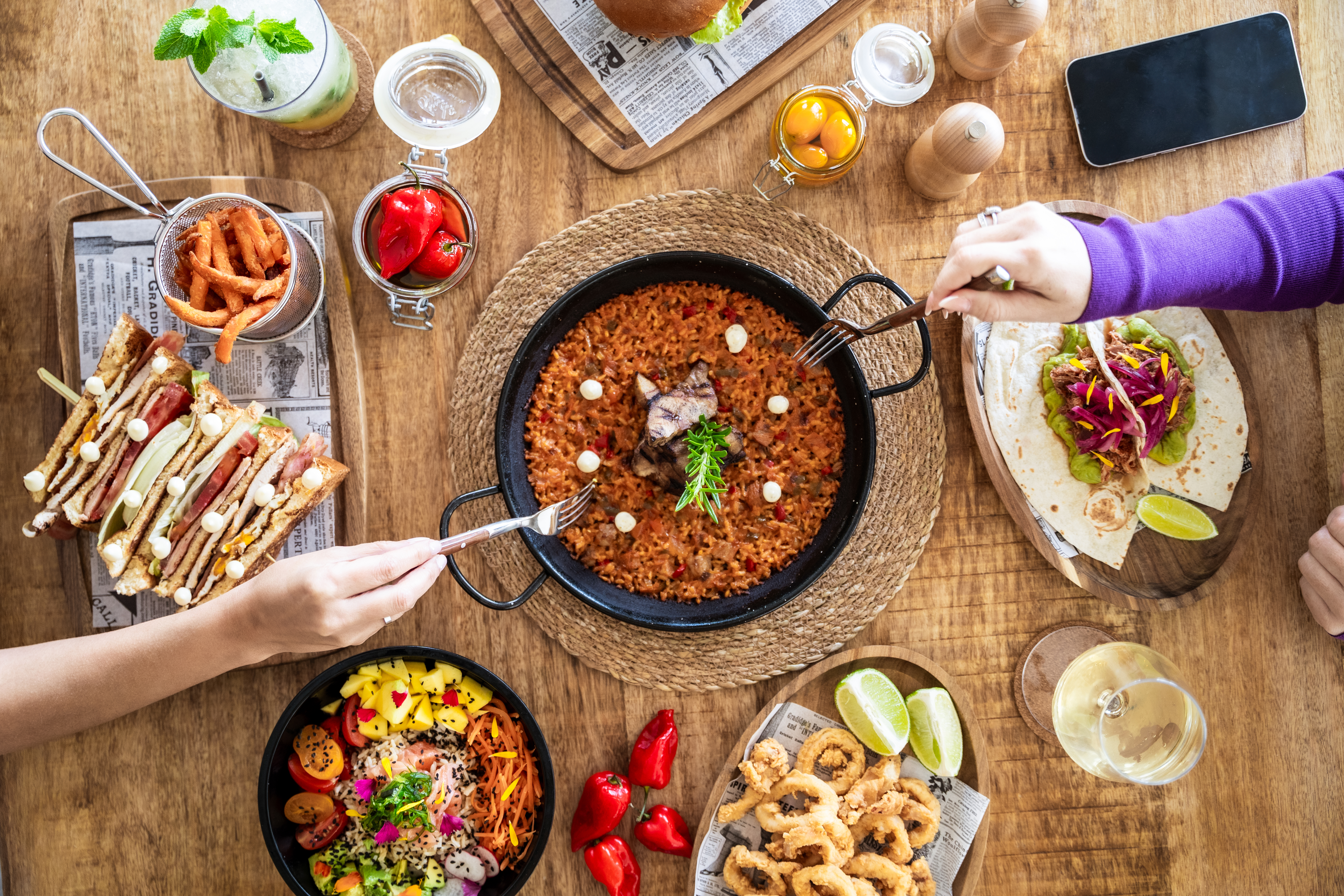 Overhead view of a restaurant table laden with paella, tapas, and drinks.