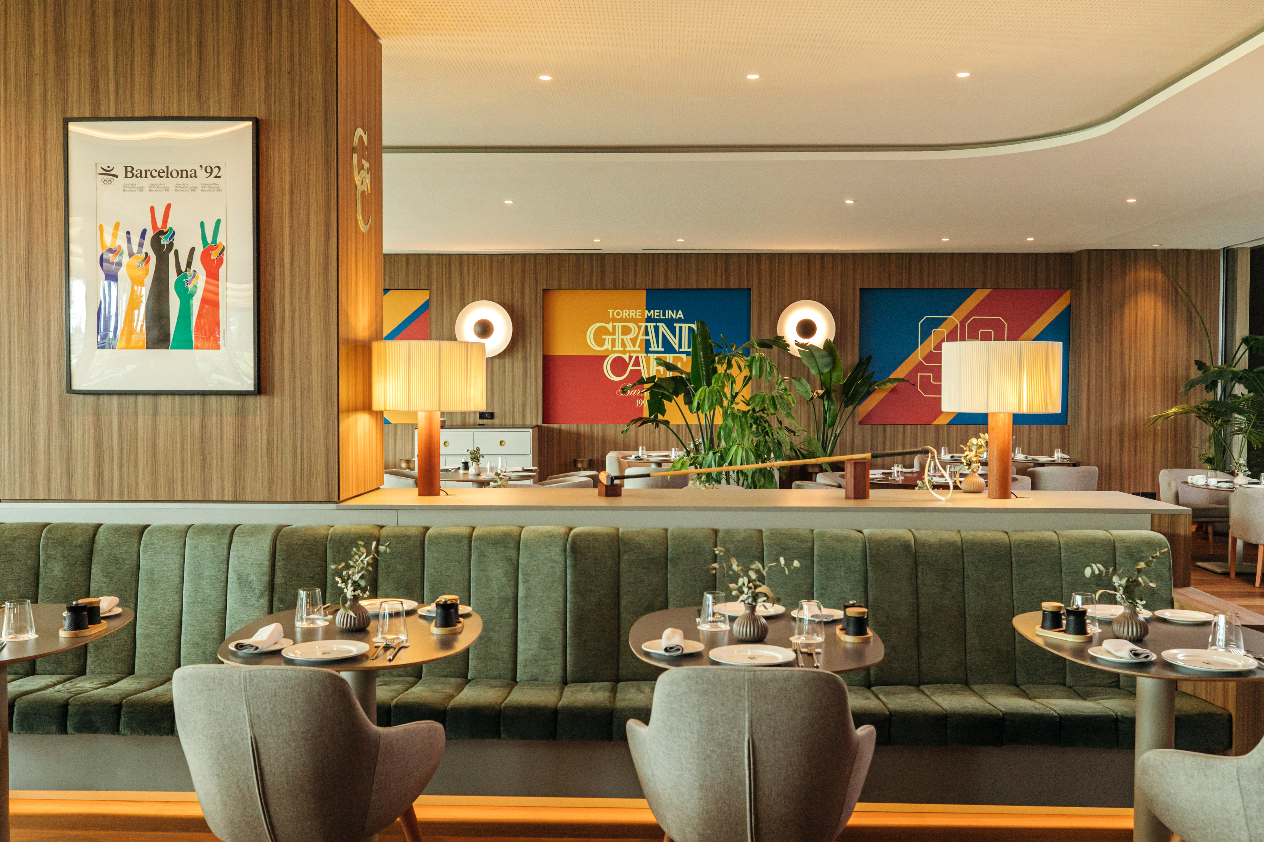 Modern dining interior with green banquettes, wood panels, and Barcelona art.