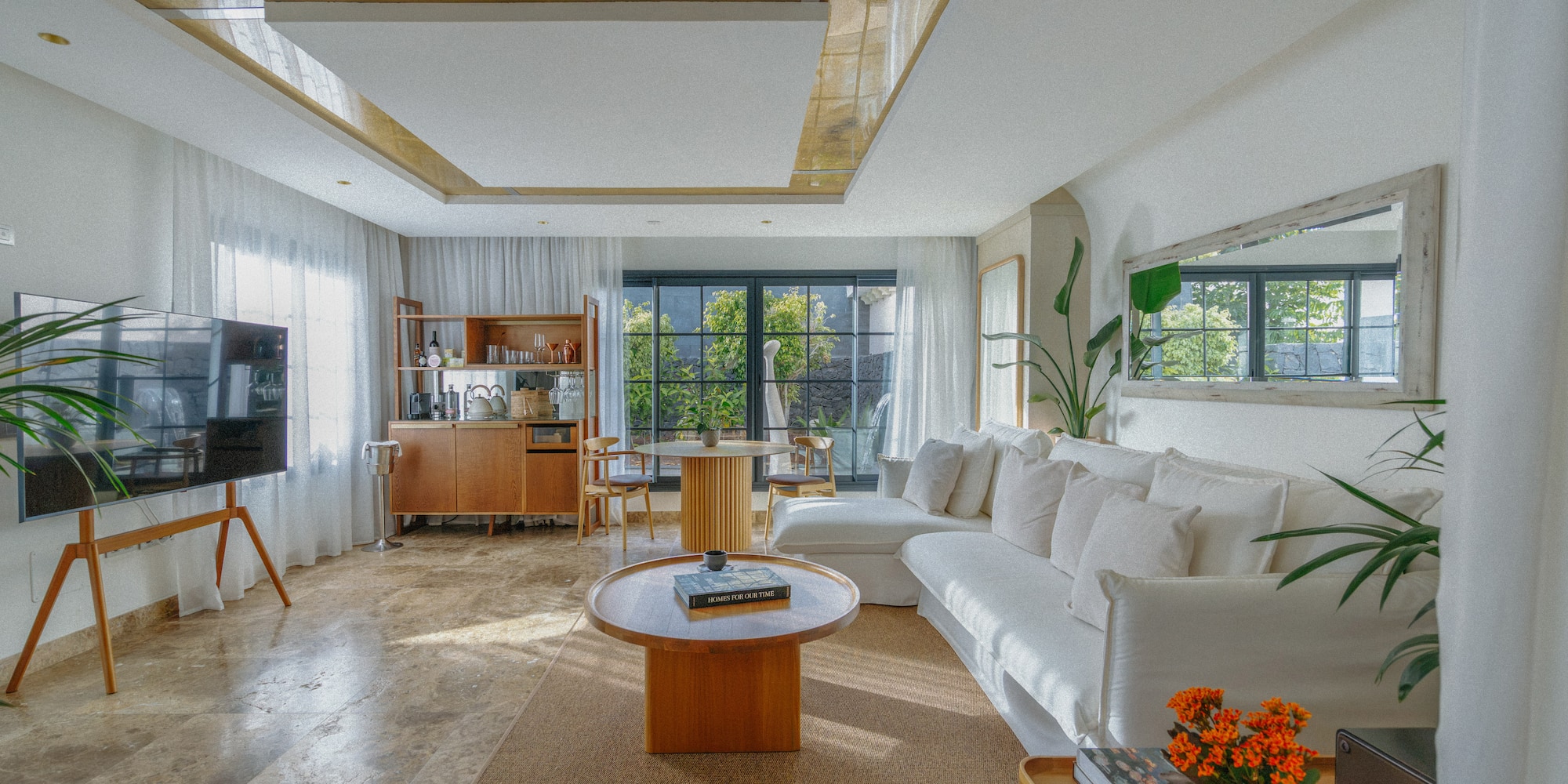 Modern living room with white sofa, wooden table, plants, natural light.