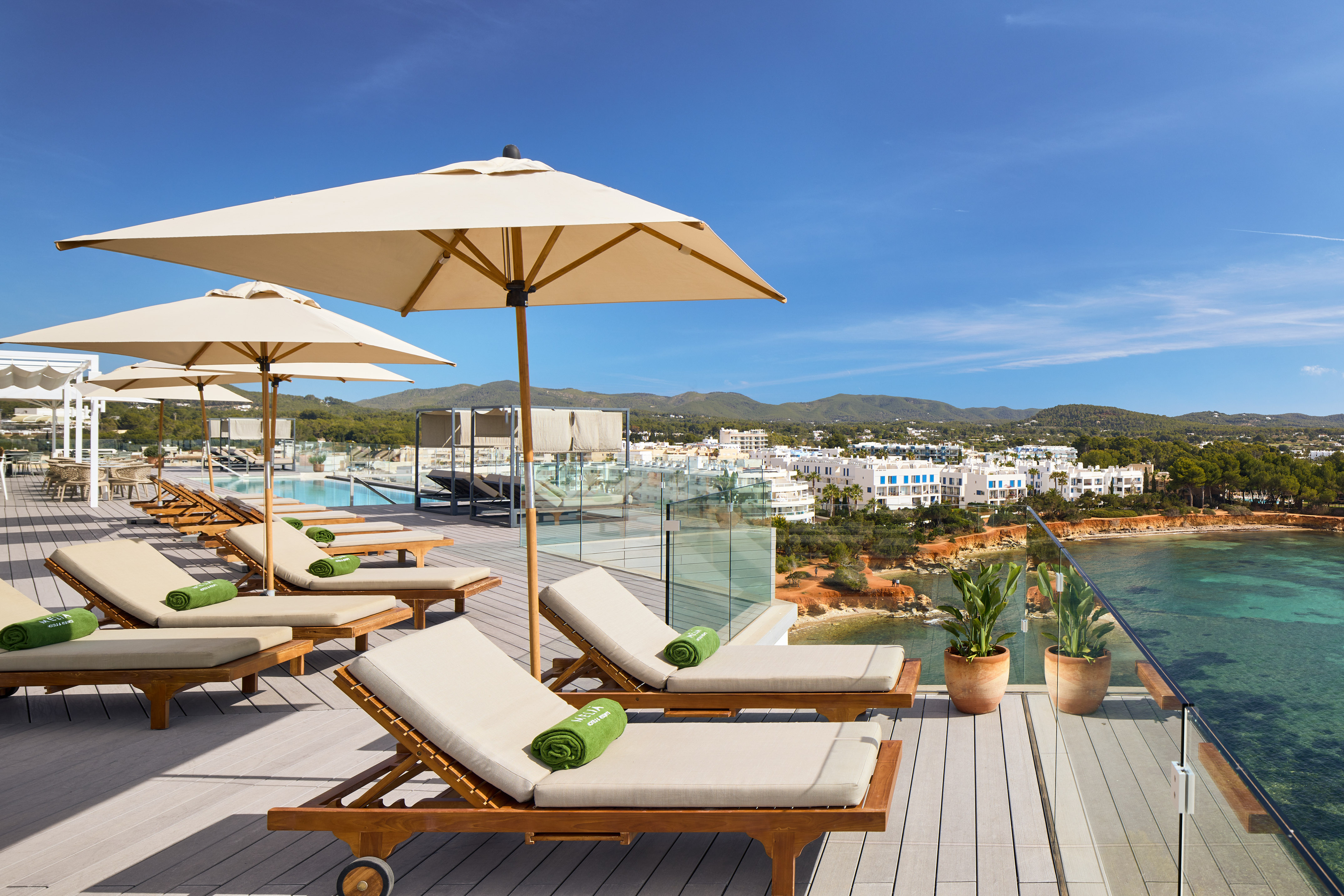 Rooftop pool and lounge area with sea view, coastal town, and clear blue sky.