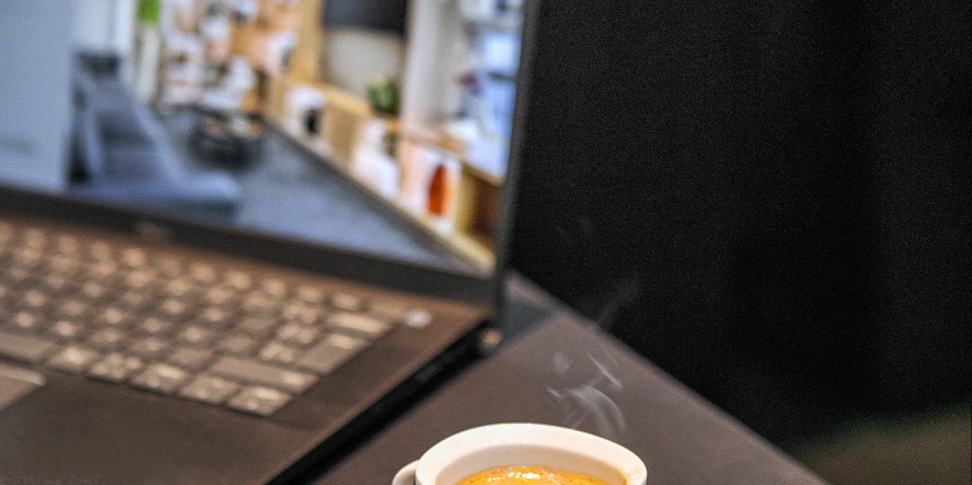 a cup of coffee on a saucer next to a laptop