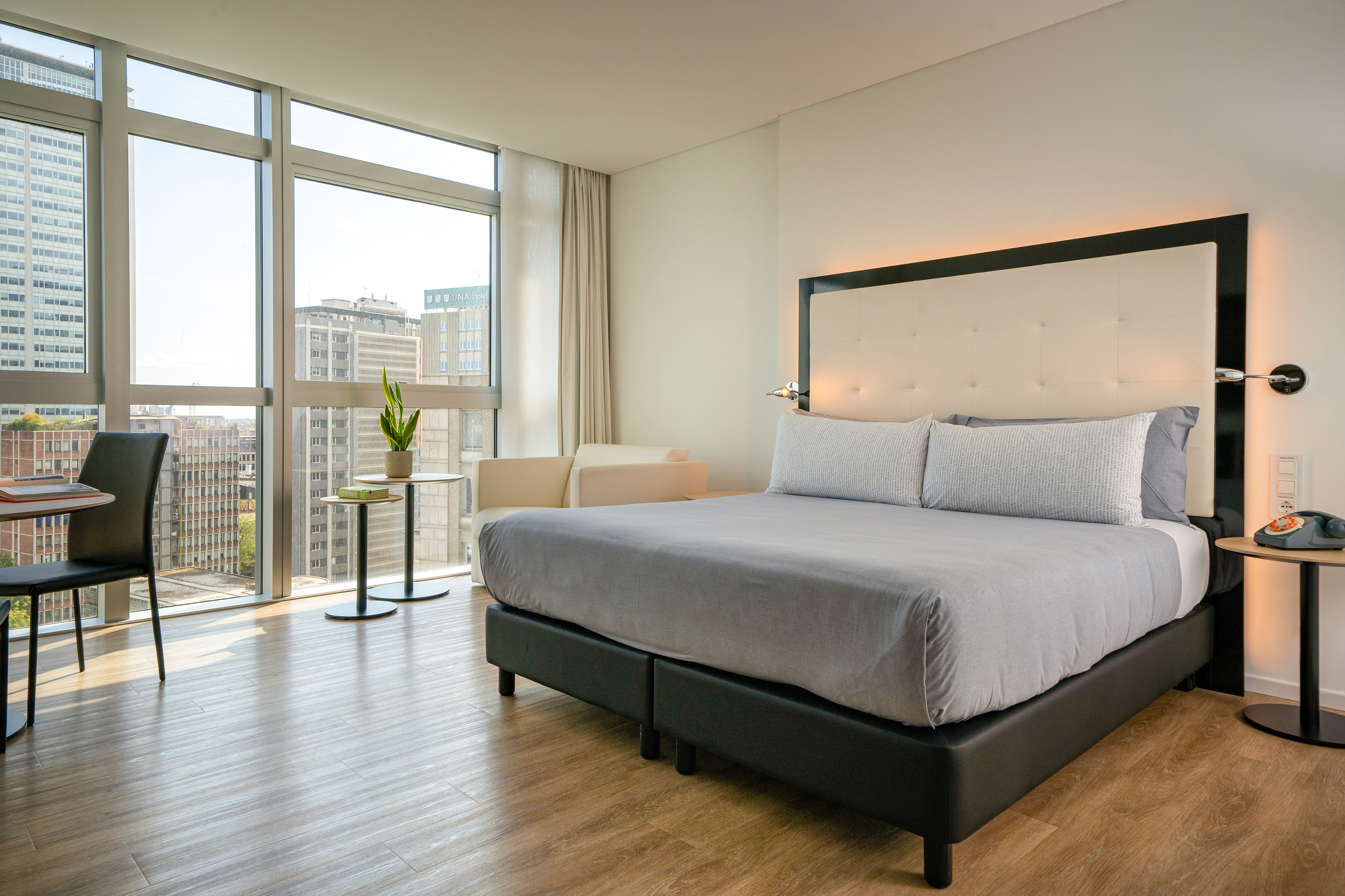 Modern hotel room with large bed, city view, and workspace.