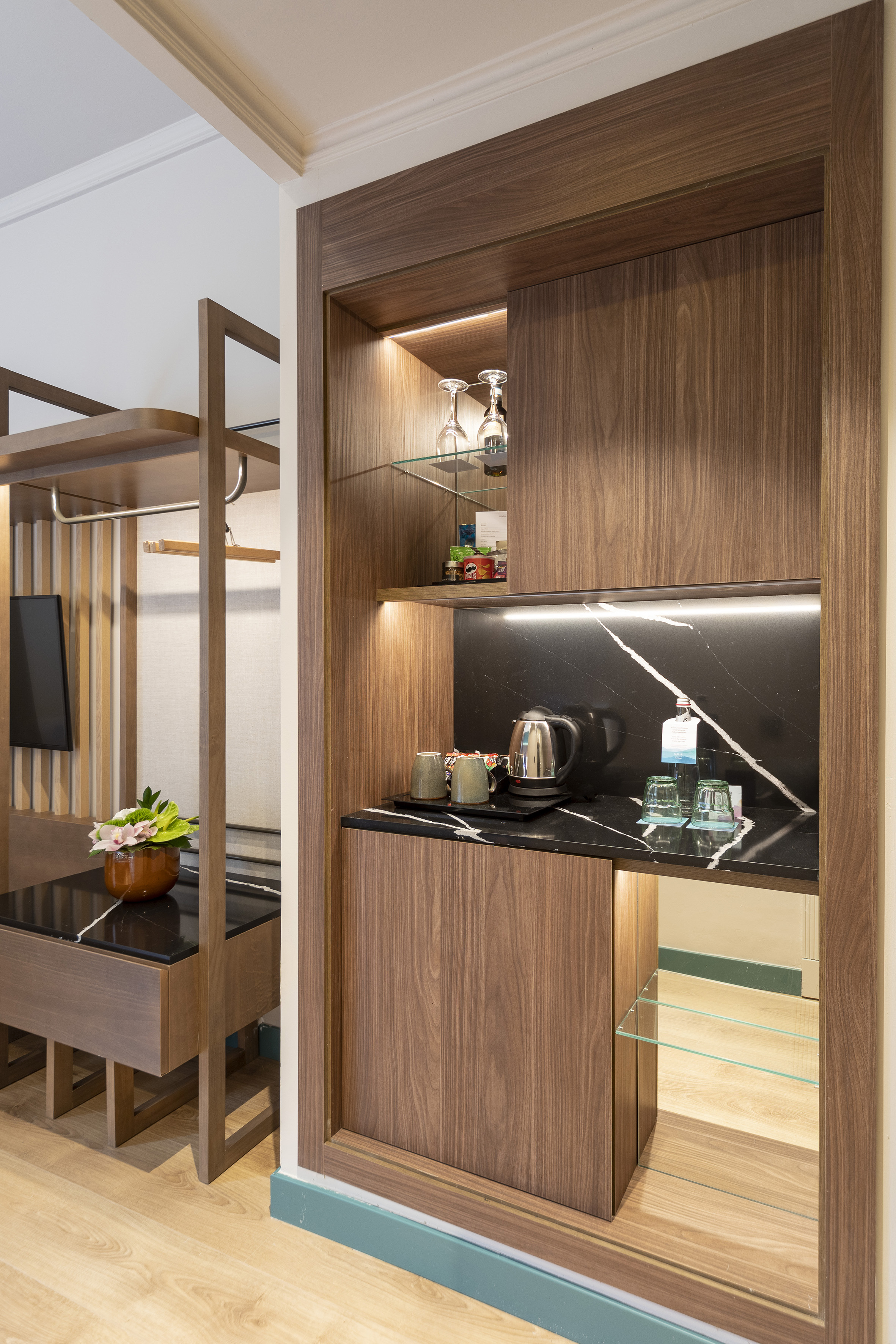 Modern hotel room mini-bar with wooden cabinet, black marble counter, kettle.
