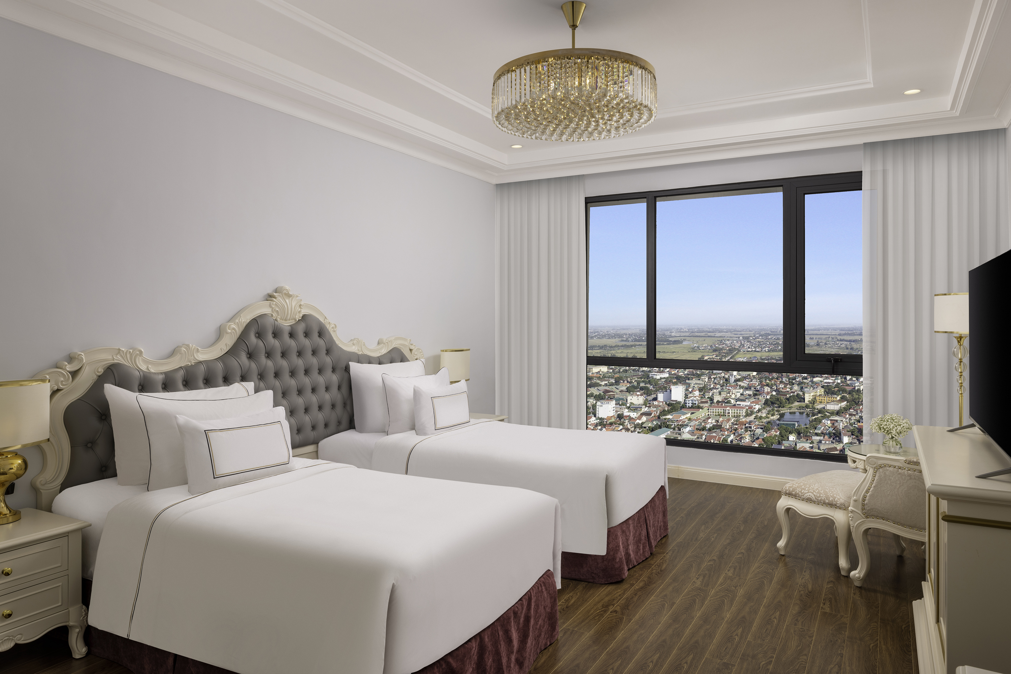 Luxury hotel twin room with city view, tufted headboards, and gold chandelier.