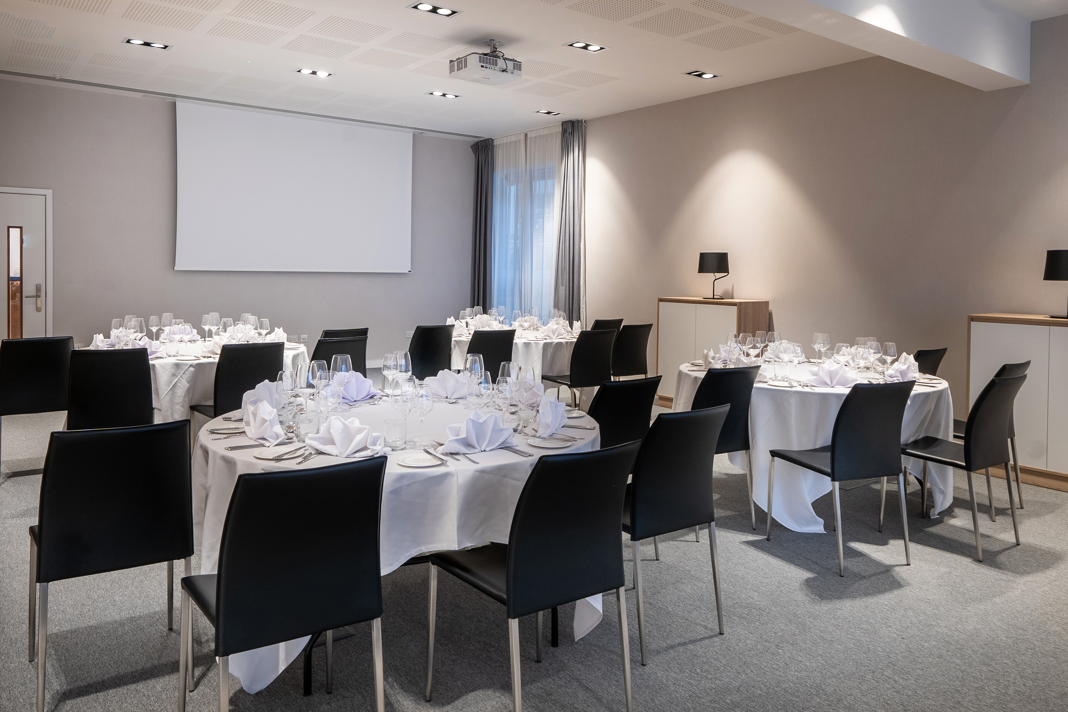 Hotel meeting room with projector screen, round tables, and formal settings.
