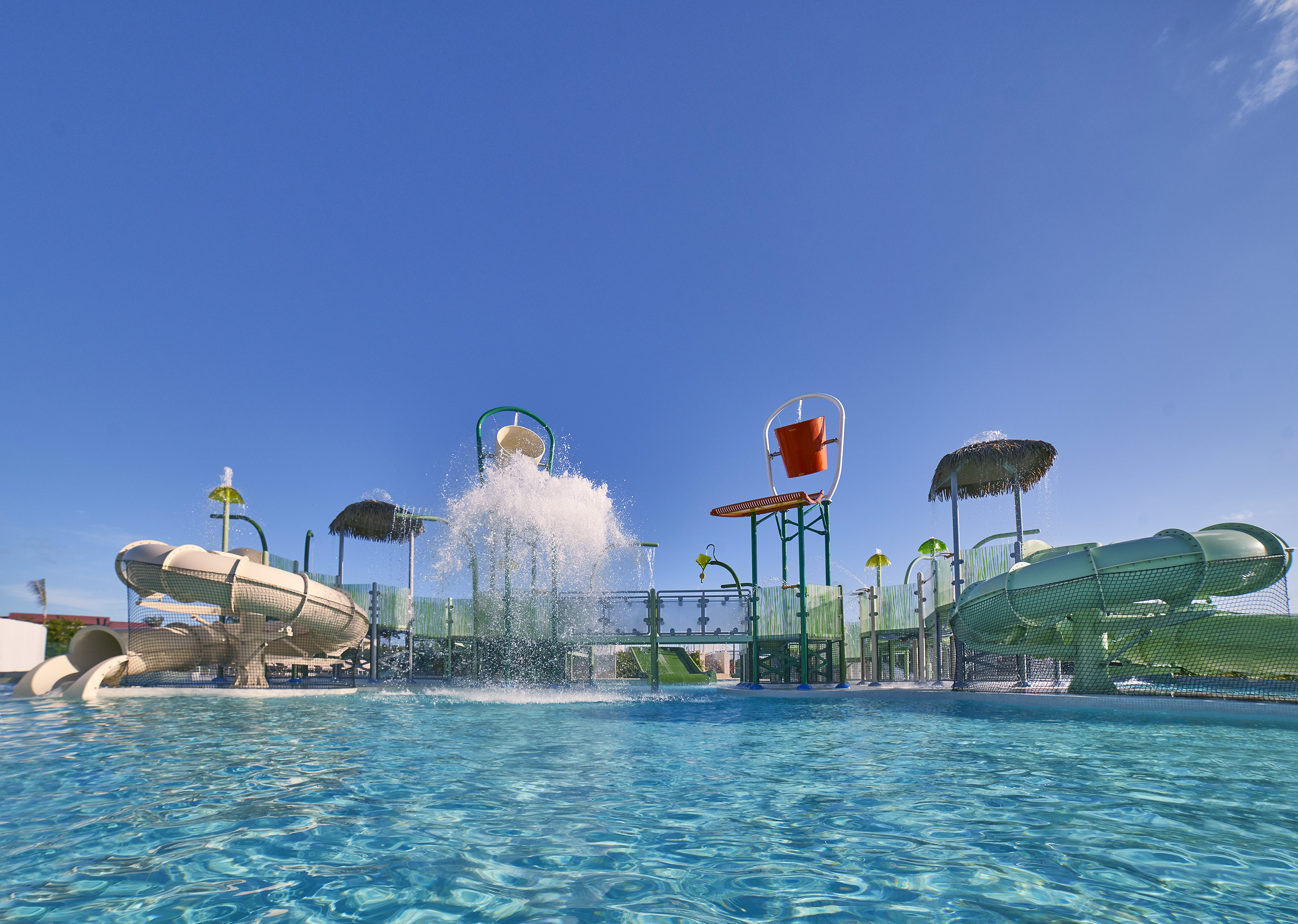Water park splash pad with slides, splashing water buckets, and clear pool.