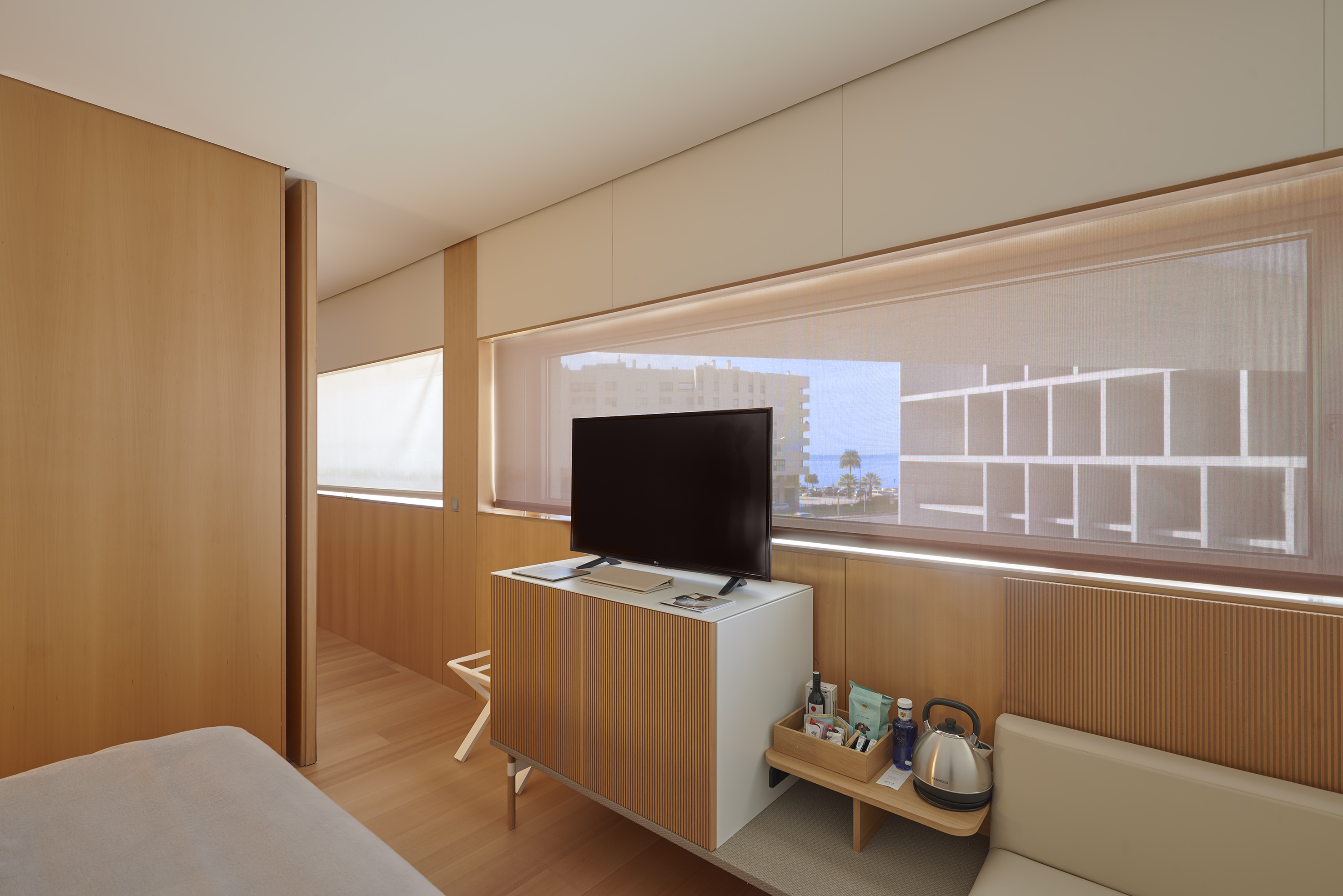 Modern hotel room with TV, wood decor, and window view of beach and sea.