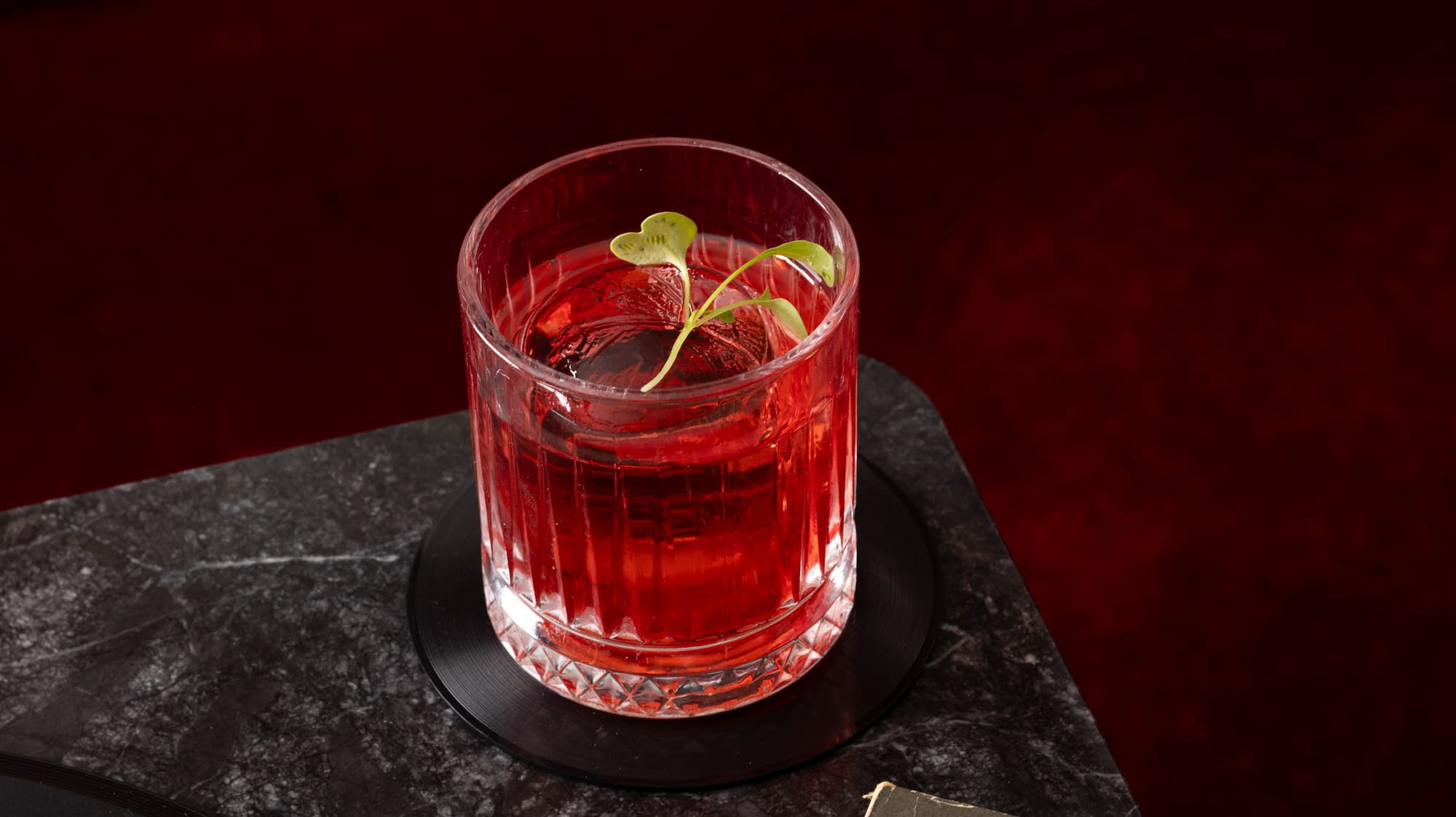 a glass of red liquid with a strawberry on top of a black surface