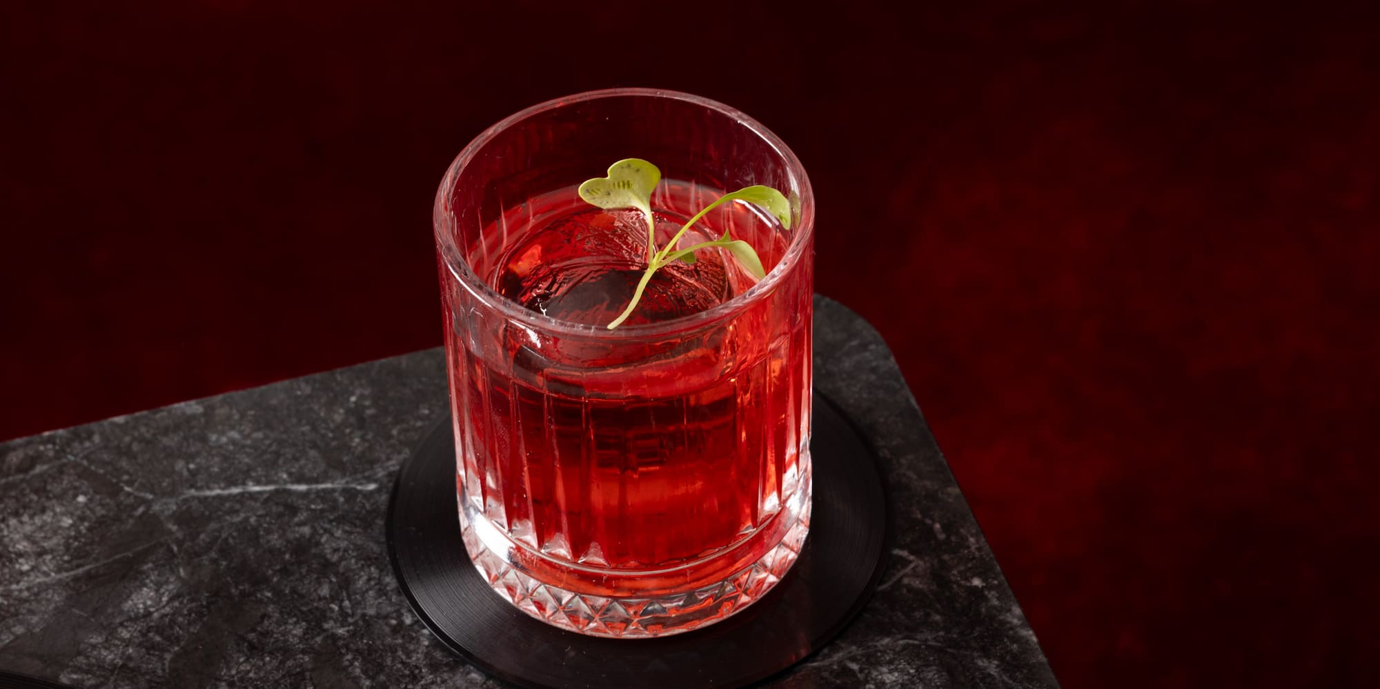 a glass of red liquid with a strawberry on top of a black surface