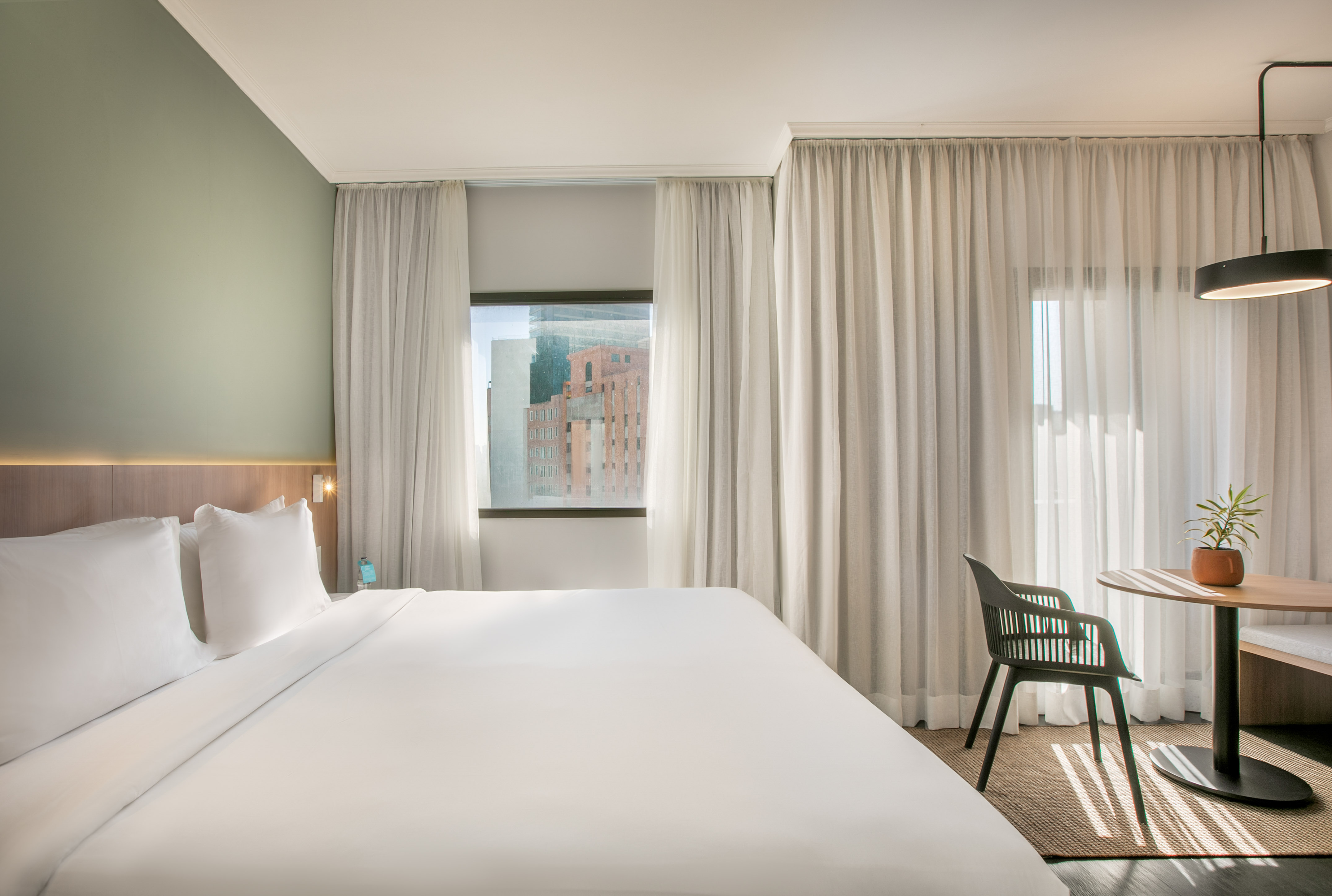 Modern hotel room, white bed, city view, green wall, and small table.