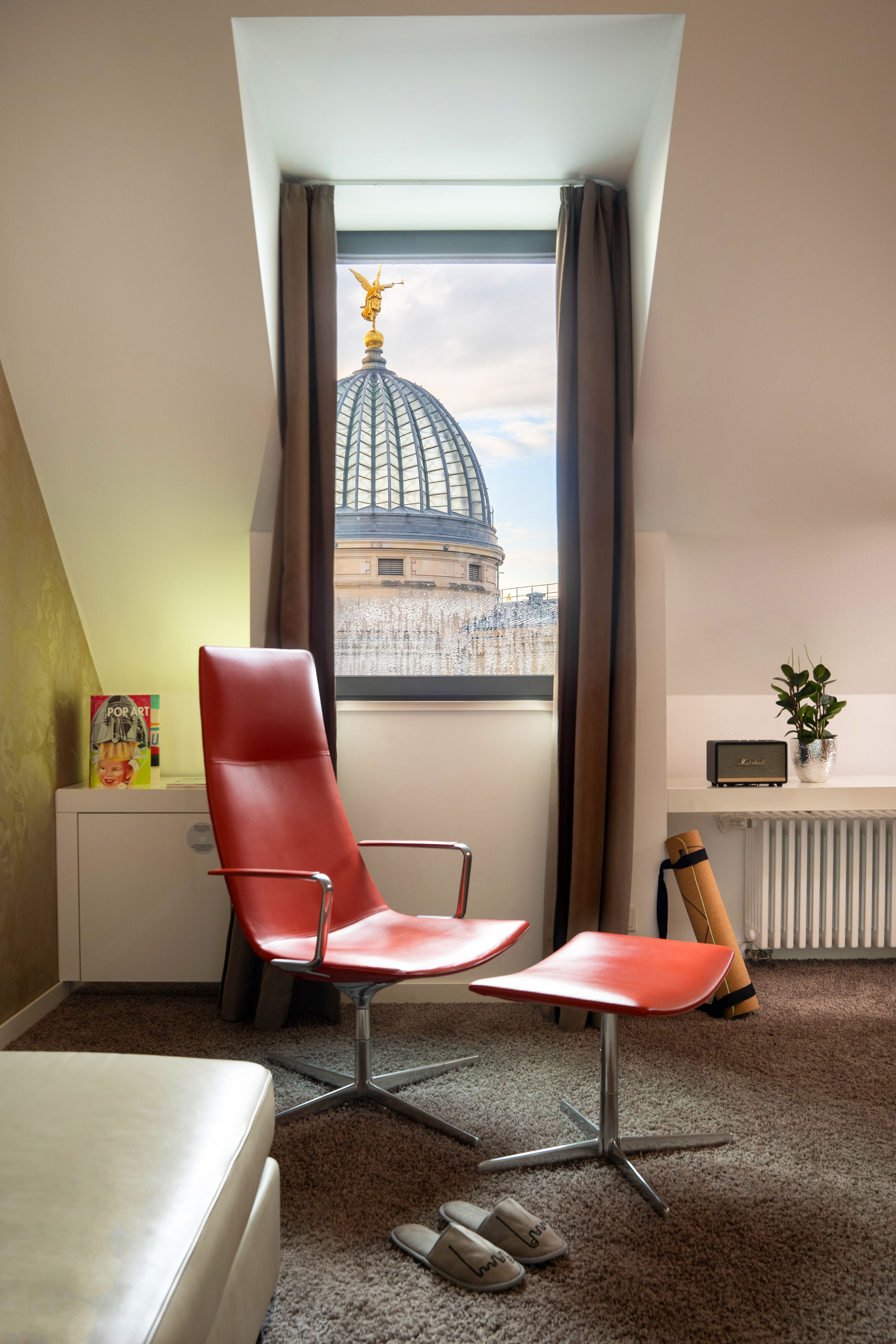 Attic room with red armchair, golden angel on large dome visible through window.