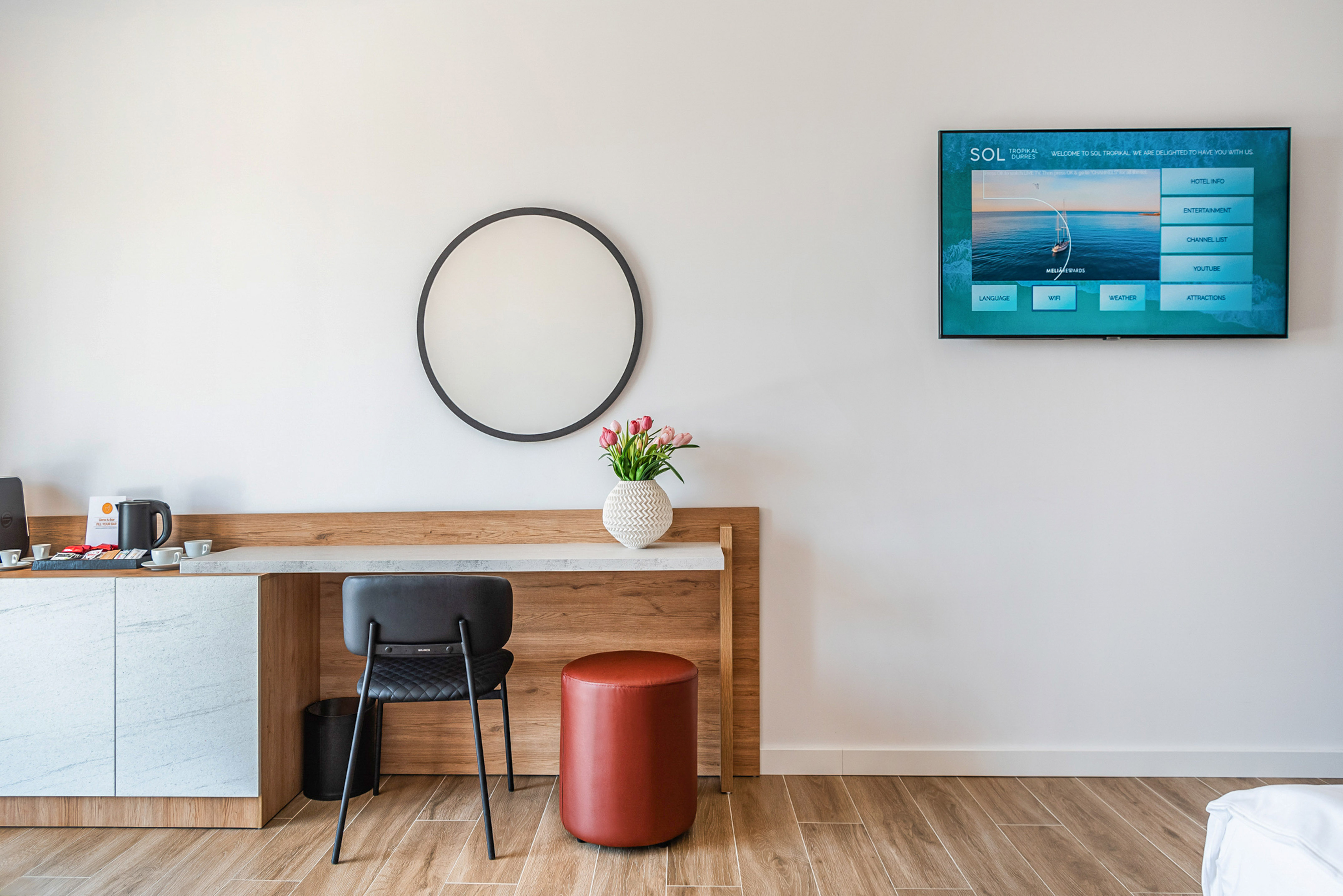 Modern Sol Tropikal hotel room: desk, round mirror, flowers, wall-mounted smart TV.