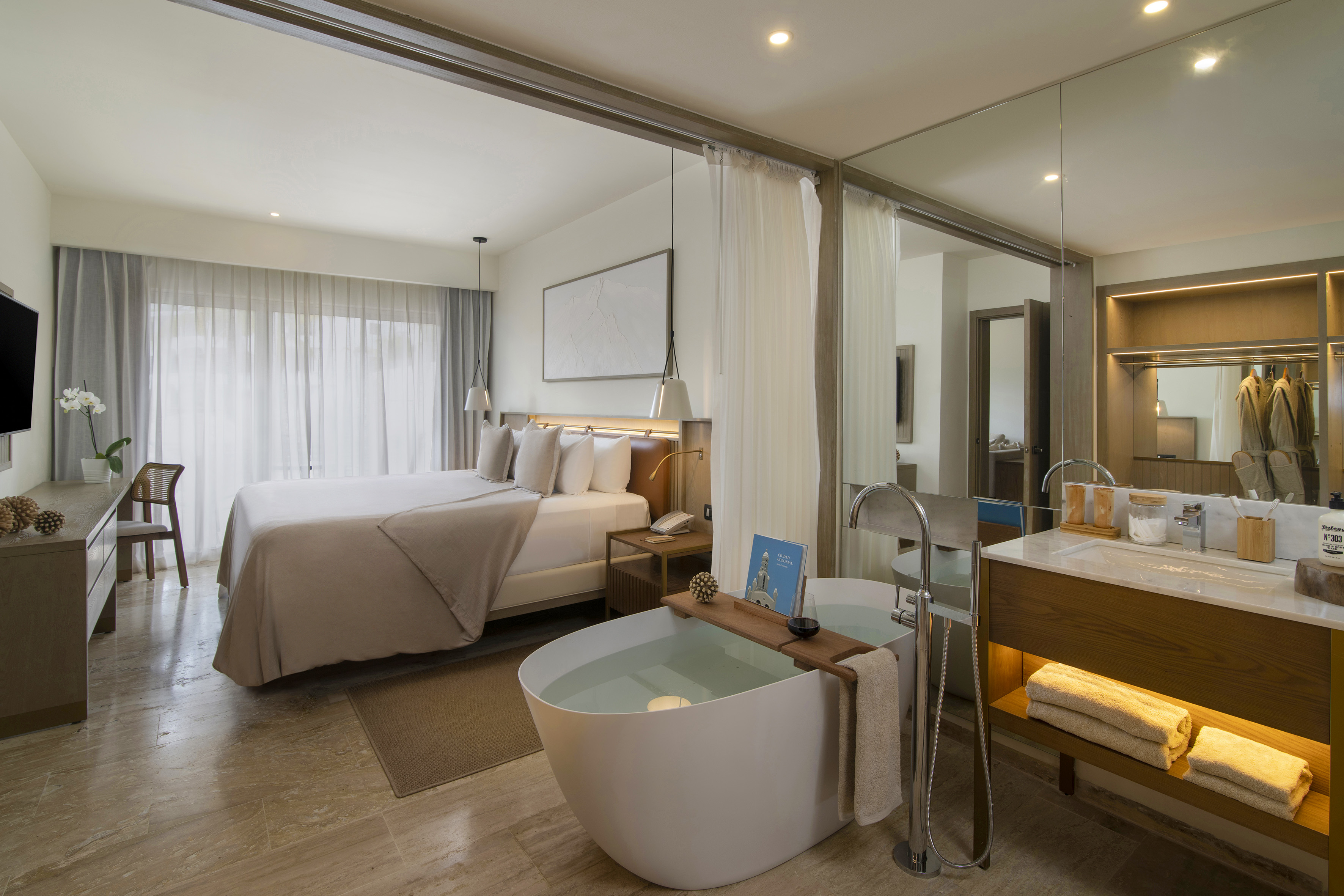 Modern hotel suite with king bed, open bathroom, and freestanding soaking tub.