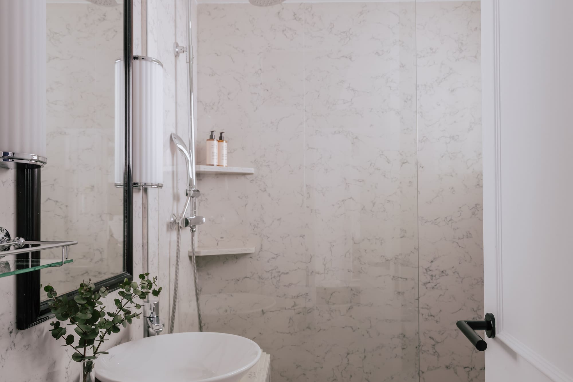 Modern white marble bathroom with vessel sink, glass shower, and sleek fixtures.