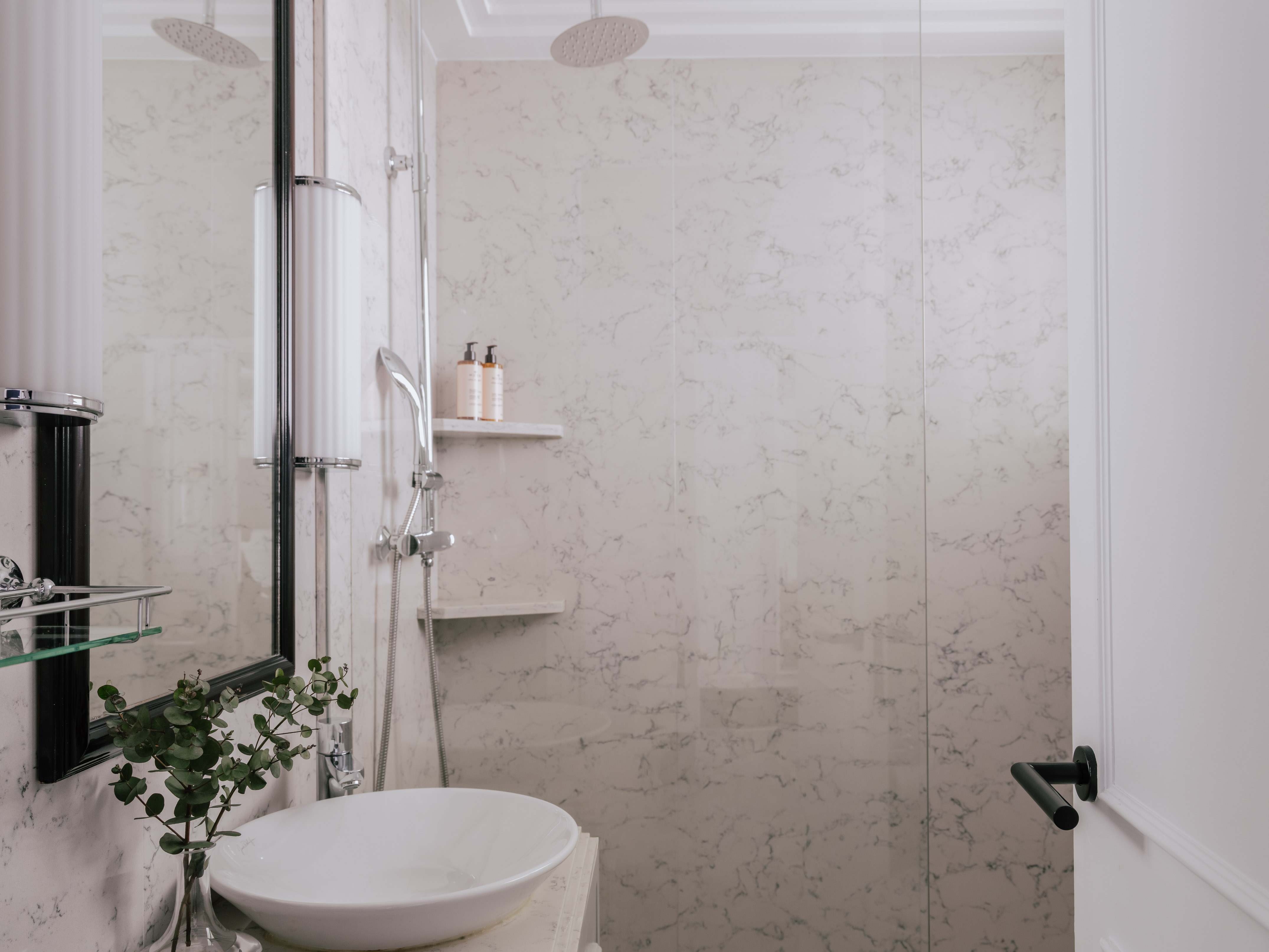 Modern white marble bathroom with vessel sink, glass shower, and sleek fixtures.