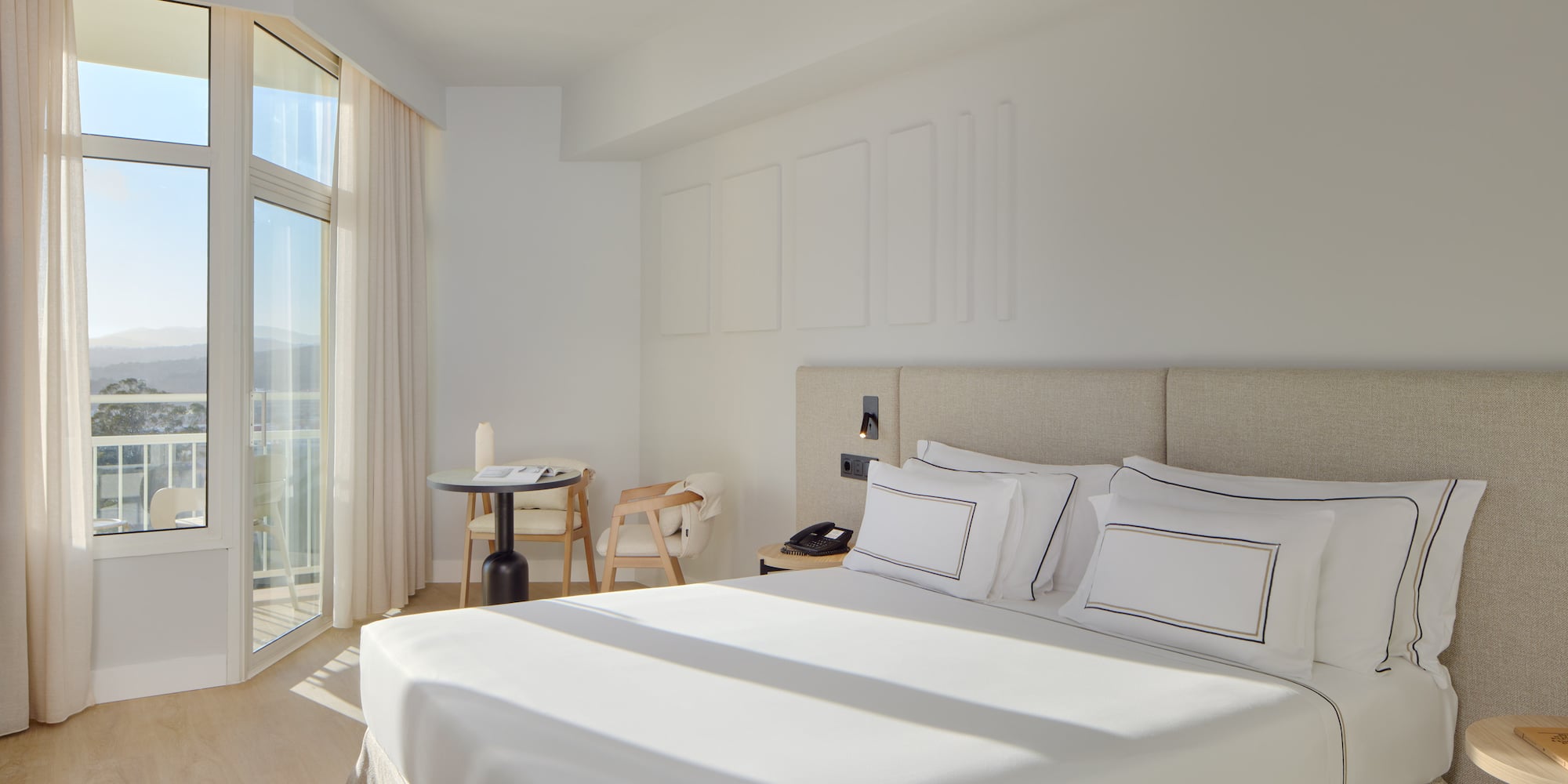 a bed with white sheets and pillows in a room with glass doors