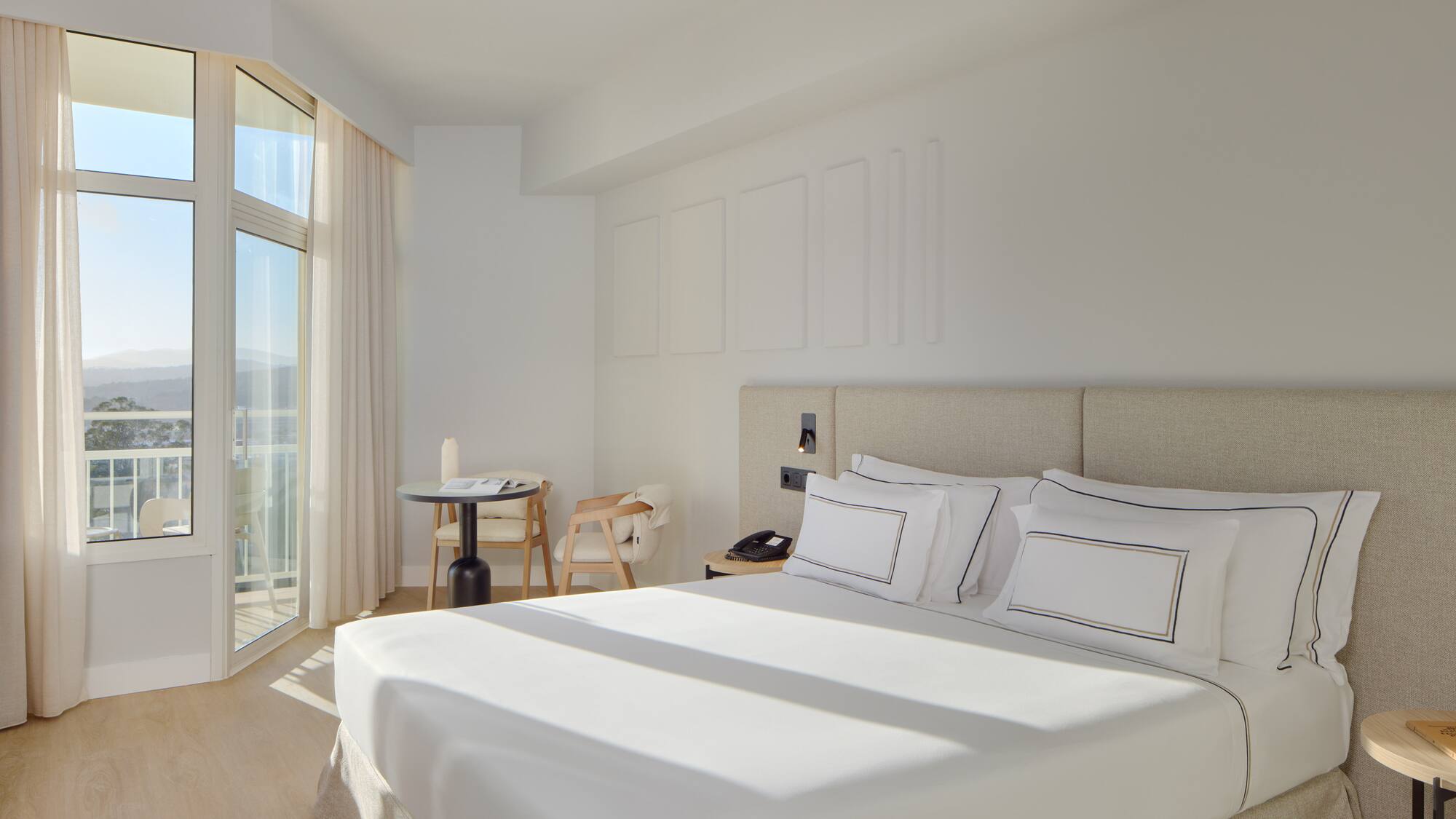 a bed with white sheets and pillows in a room with glass doors