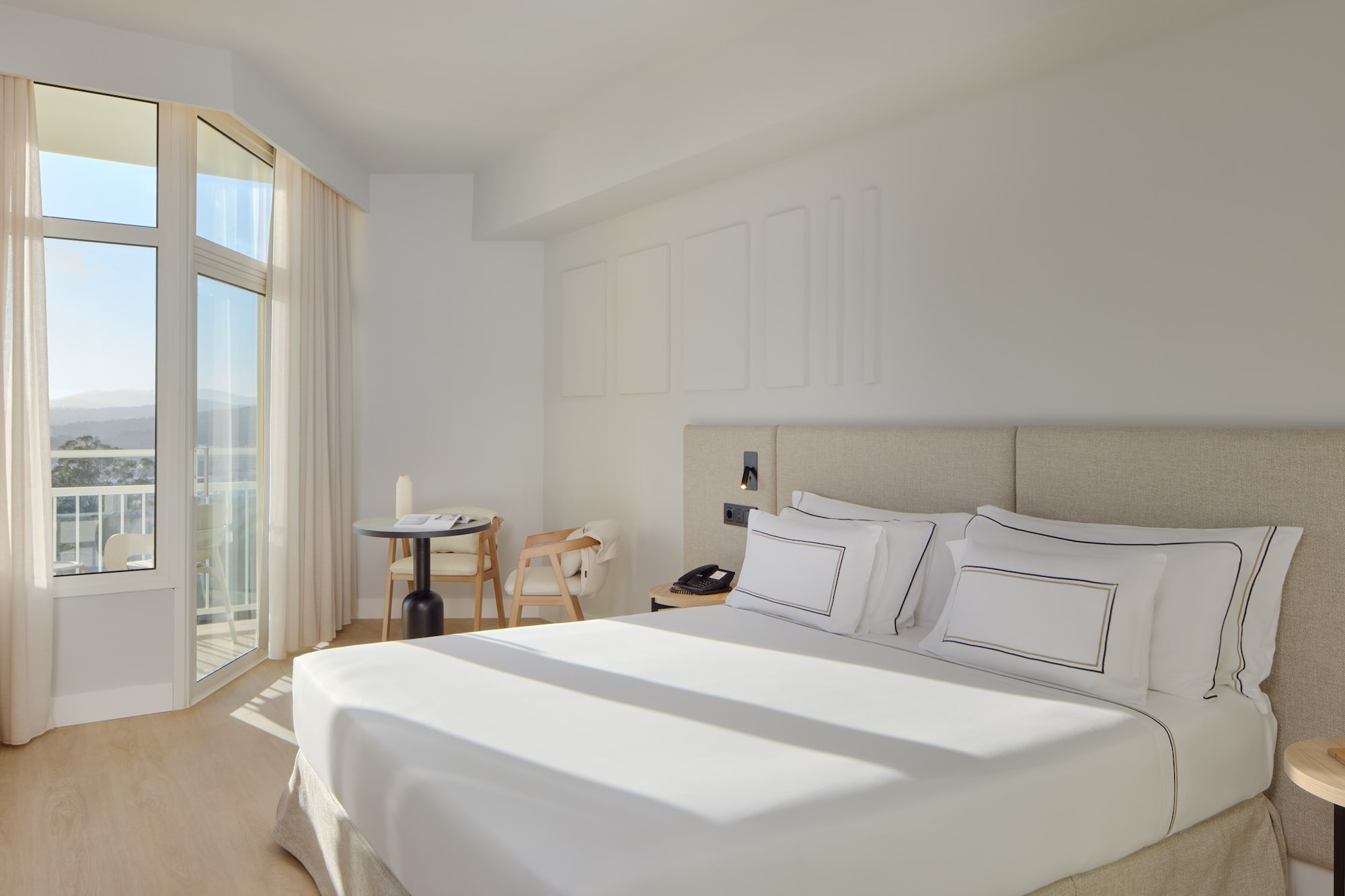 a bed with white sheets and pillows in a room with glass doors