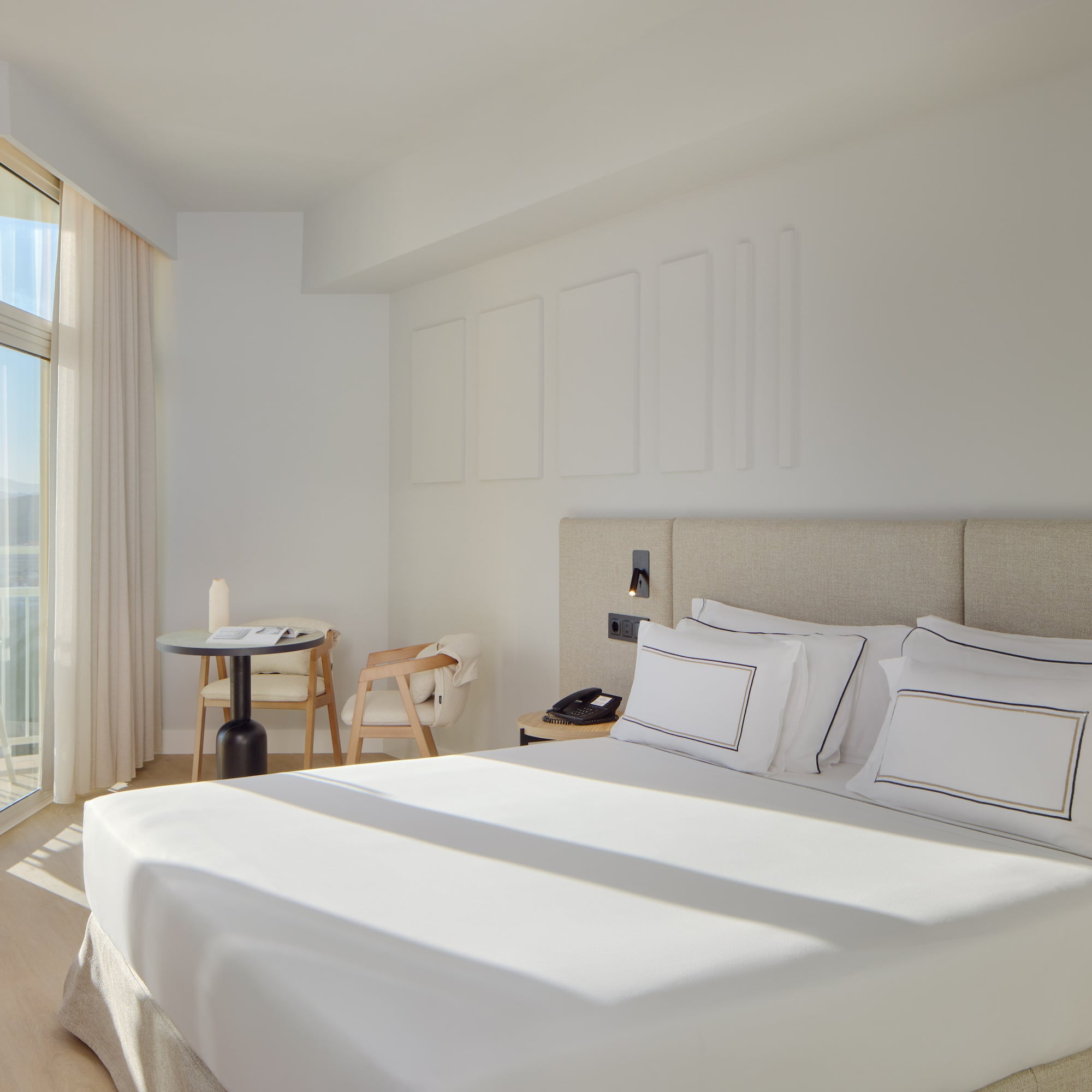 a bed with white sheets and pillows in a room with glass doors