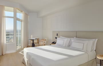 a bed with white sheets and pillows in a room with glass doors