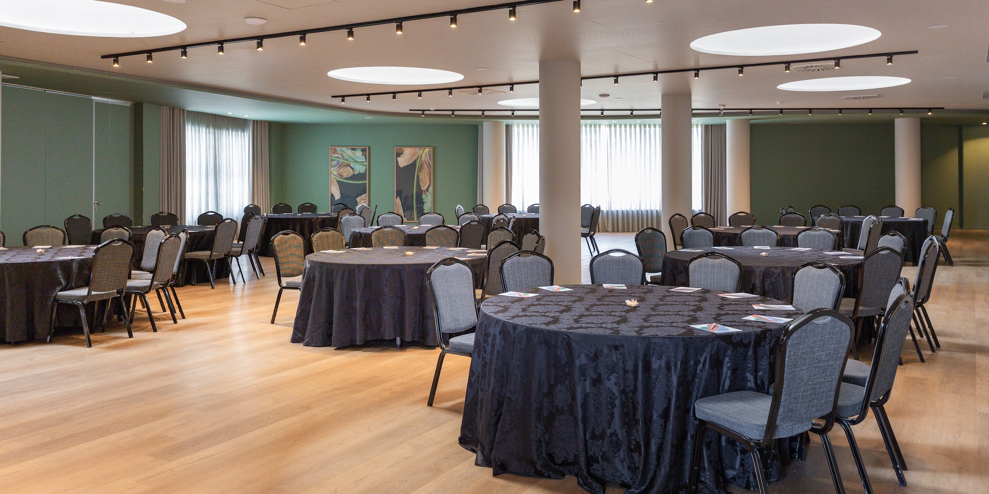 Hotel meeting room with round banquet tables, dark linens, grey chairs.