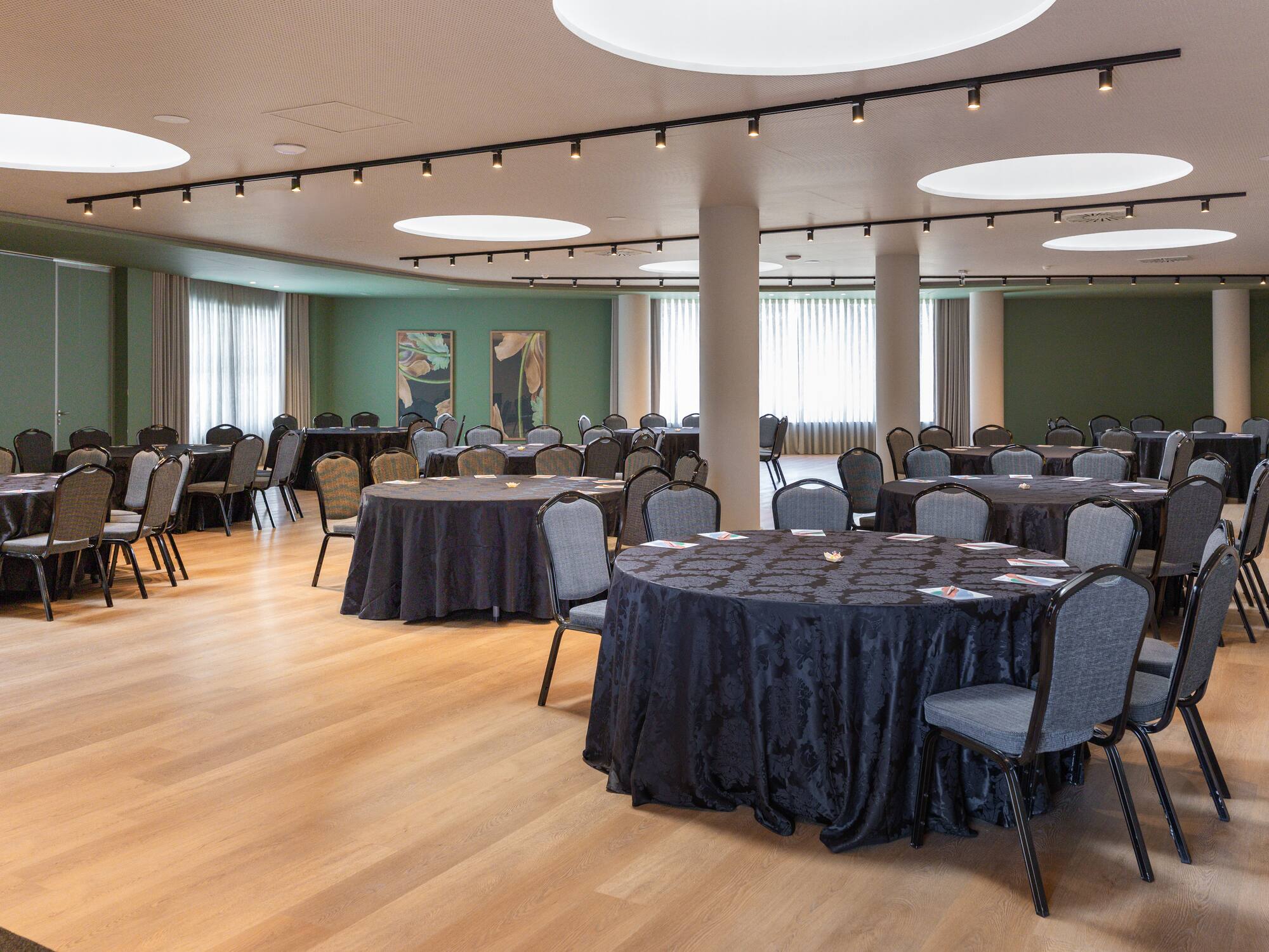 Modern conference room setup with round tables, dark linens, and grey chairs.