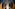 Woman in white dress looking back in modern arched hotel hallway.