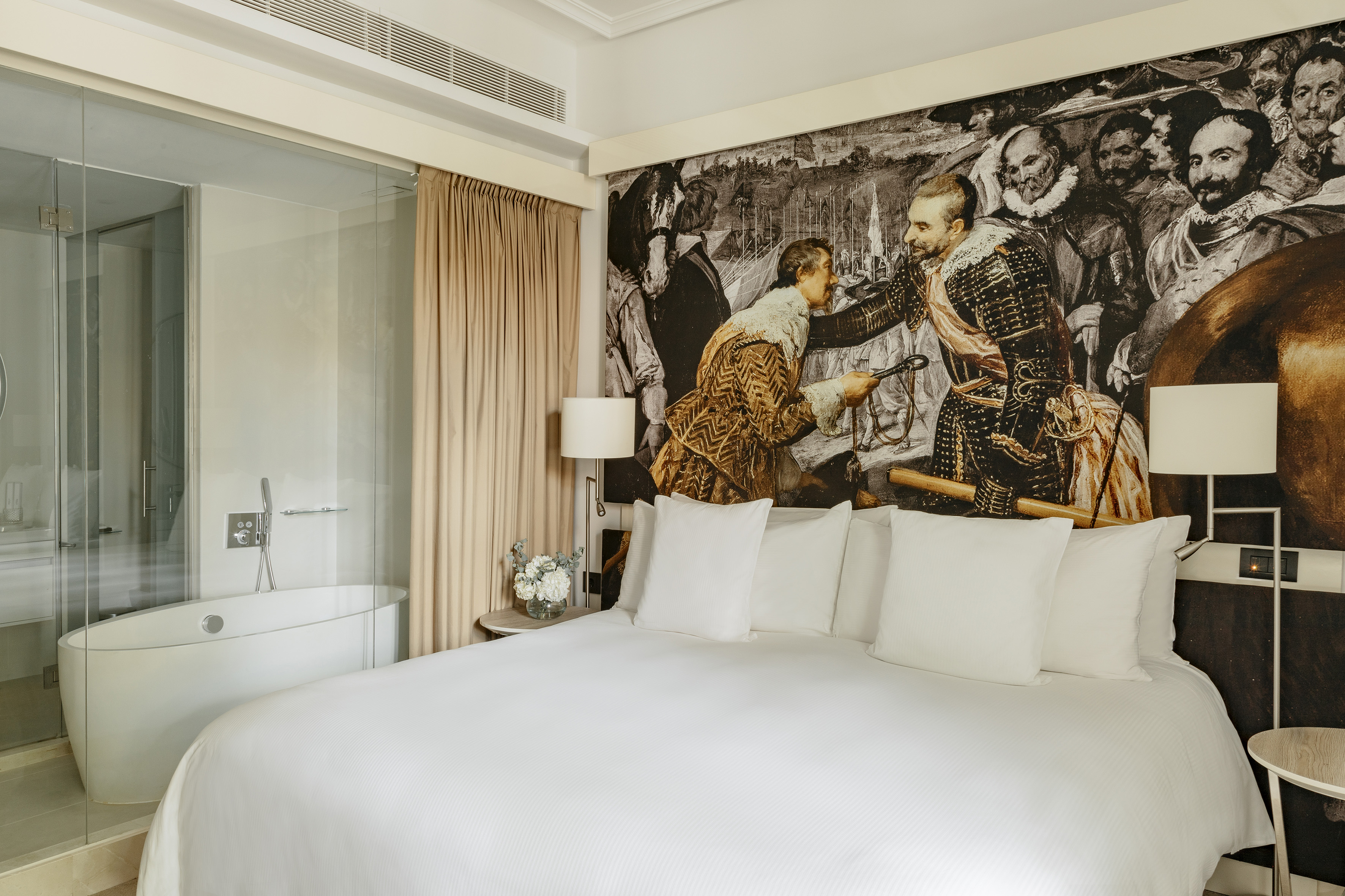 Modern hotel room with historical mural wall, king bed, and freestanding bathtub.